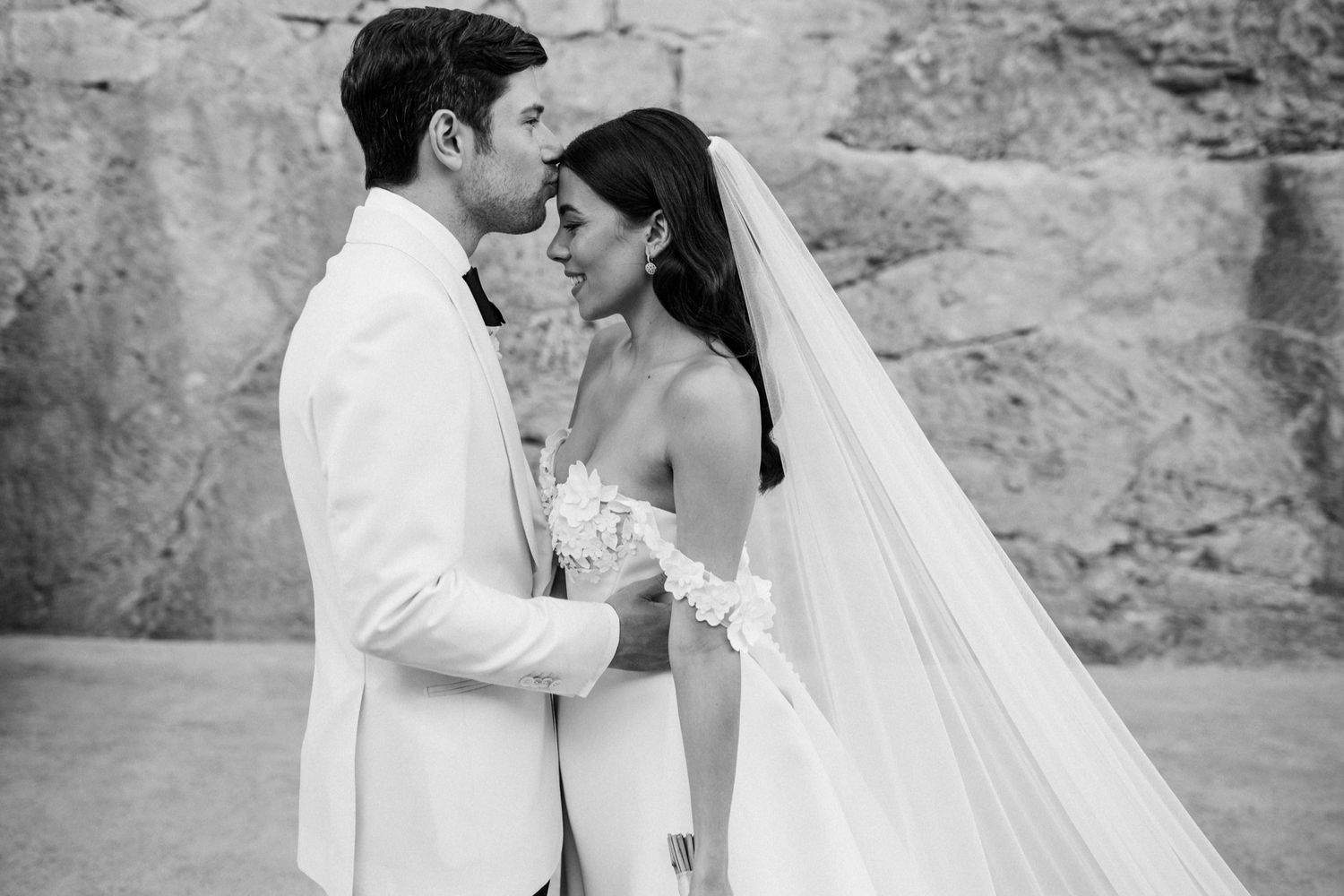 Black and white wedding photo of bride and groom sharing intimate moment, bride in veil holding bouquet.