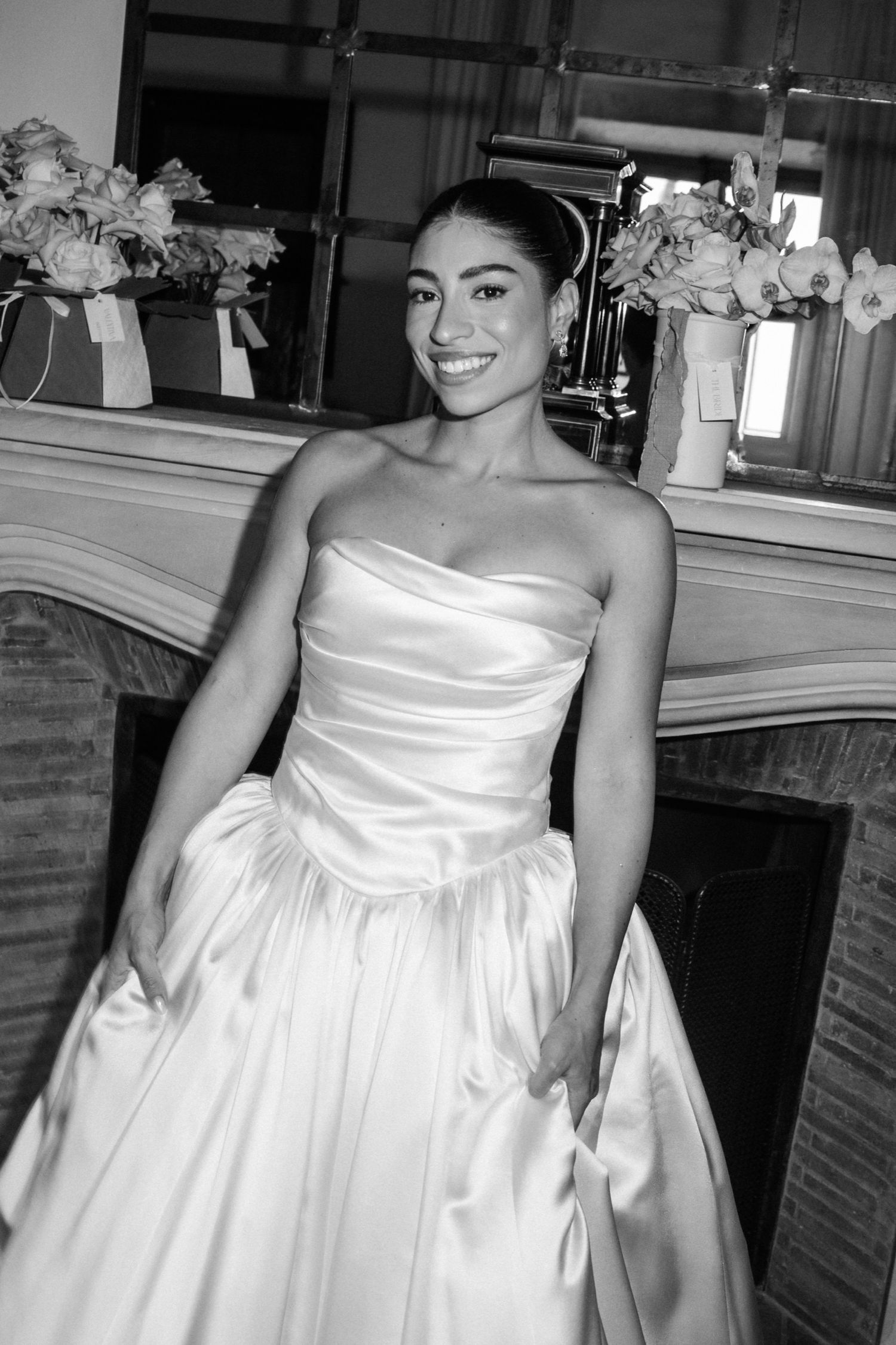 A series of black and white photos showing someone in an elegant white strapless wedding dress posing against a wall.