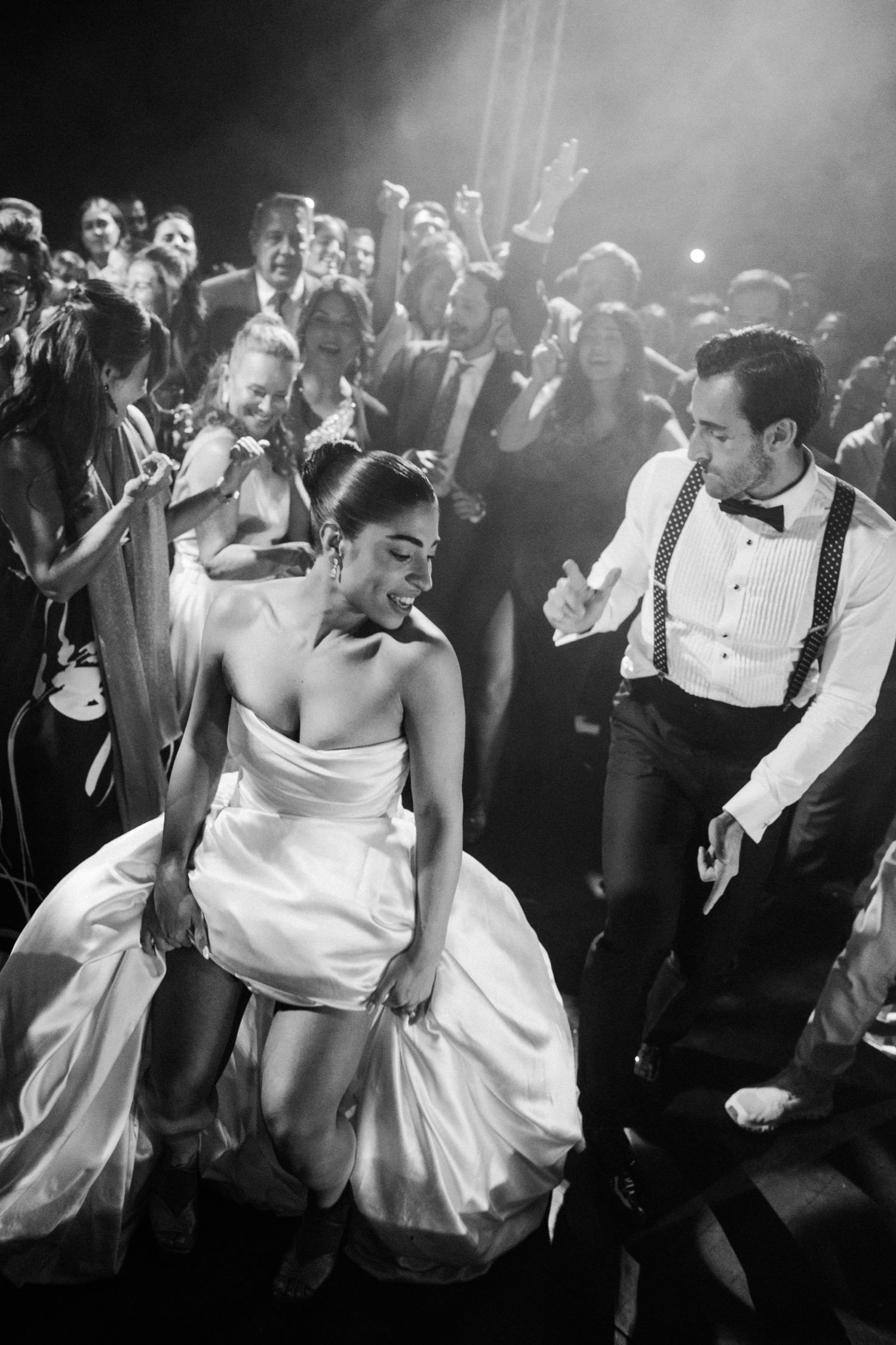Wedding guests dance energetically at a reception with dramatic lighting and smoke effects on the dance floor.