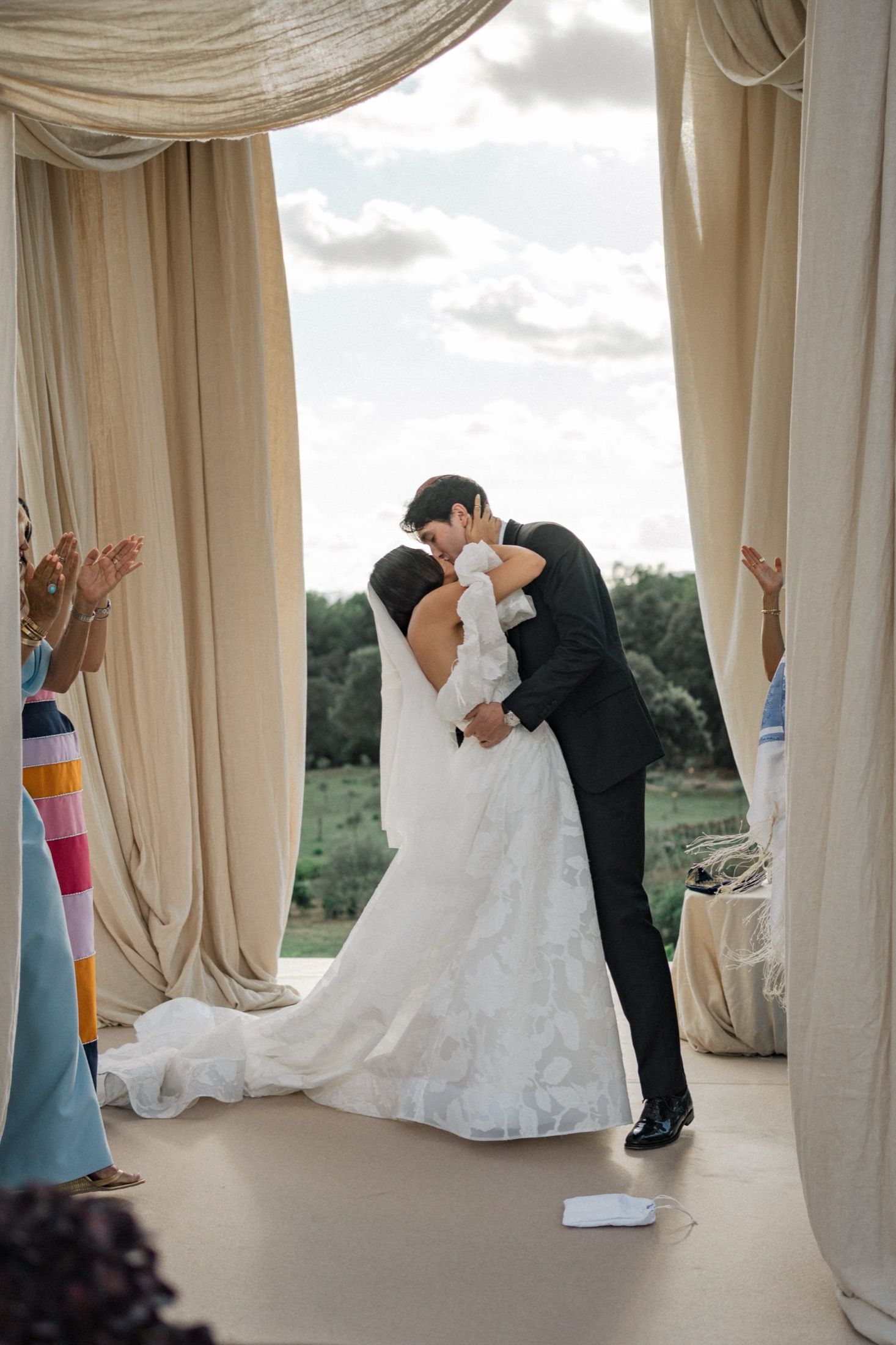 Romantic wedding ceremony moment under flowing cream-colored drapes with guests watching.