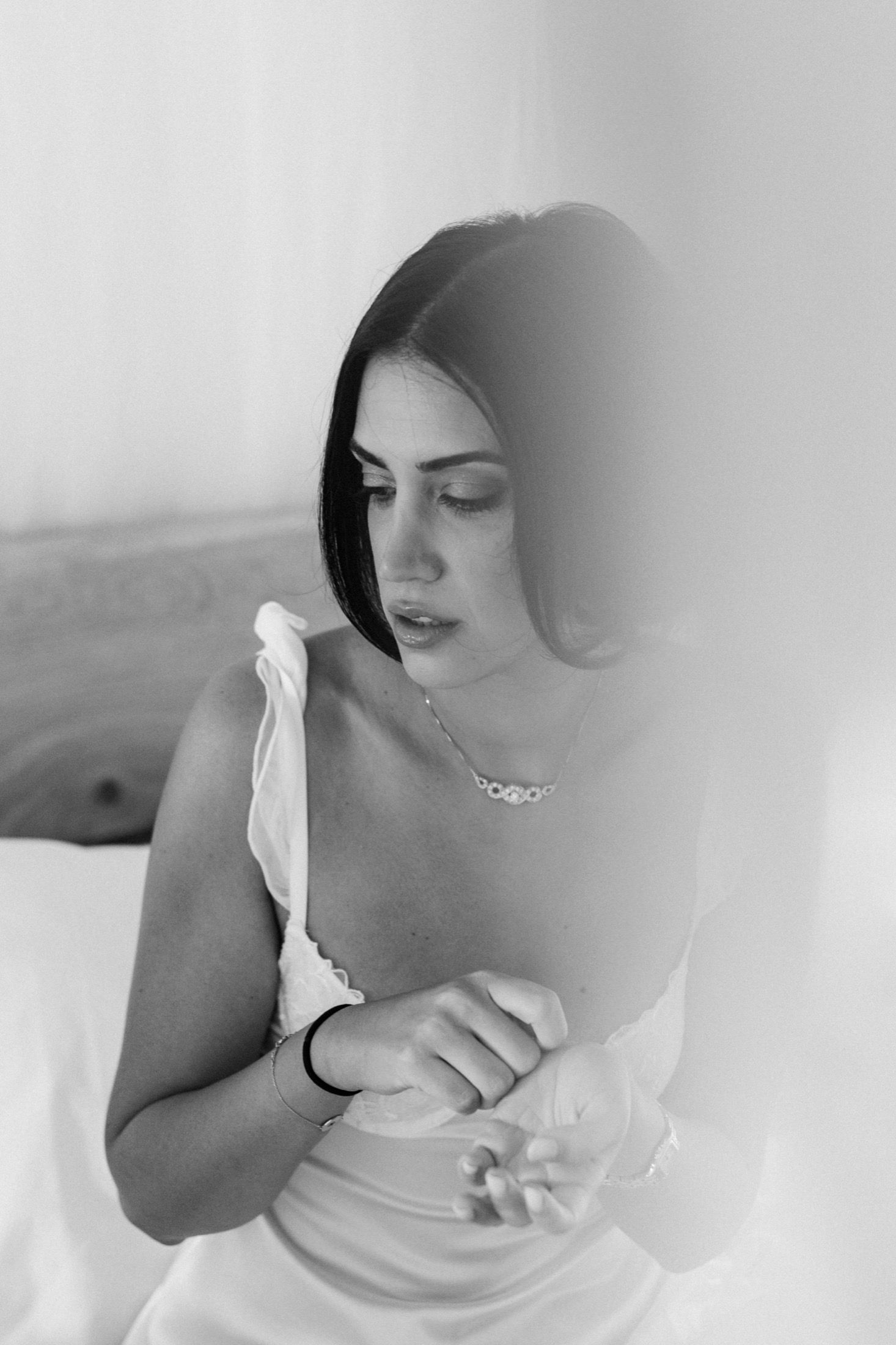 A series of soft black and white photos showing a woman in a white dress reclining on a bed.