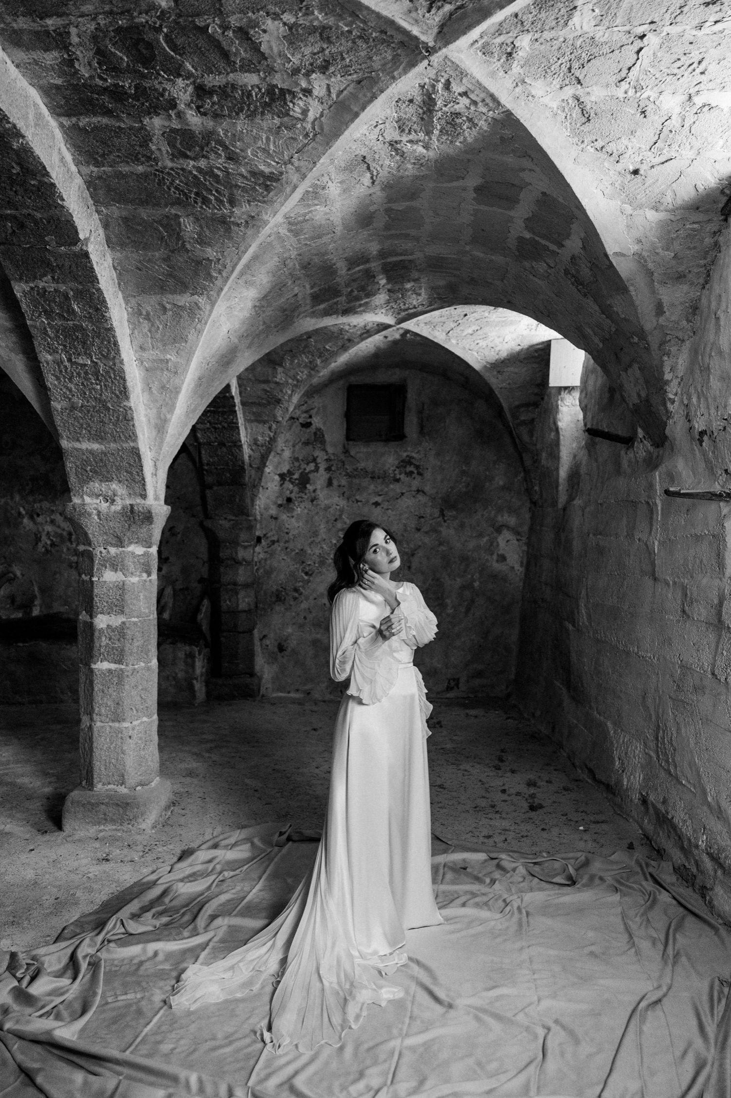 A series of black and white photos showing figures in white dresses exploring a dark stone cellar with arched ceilings.