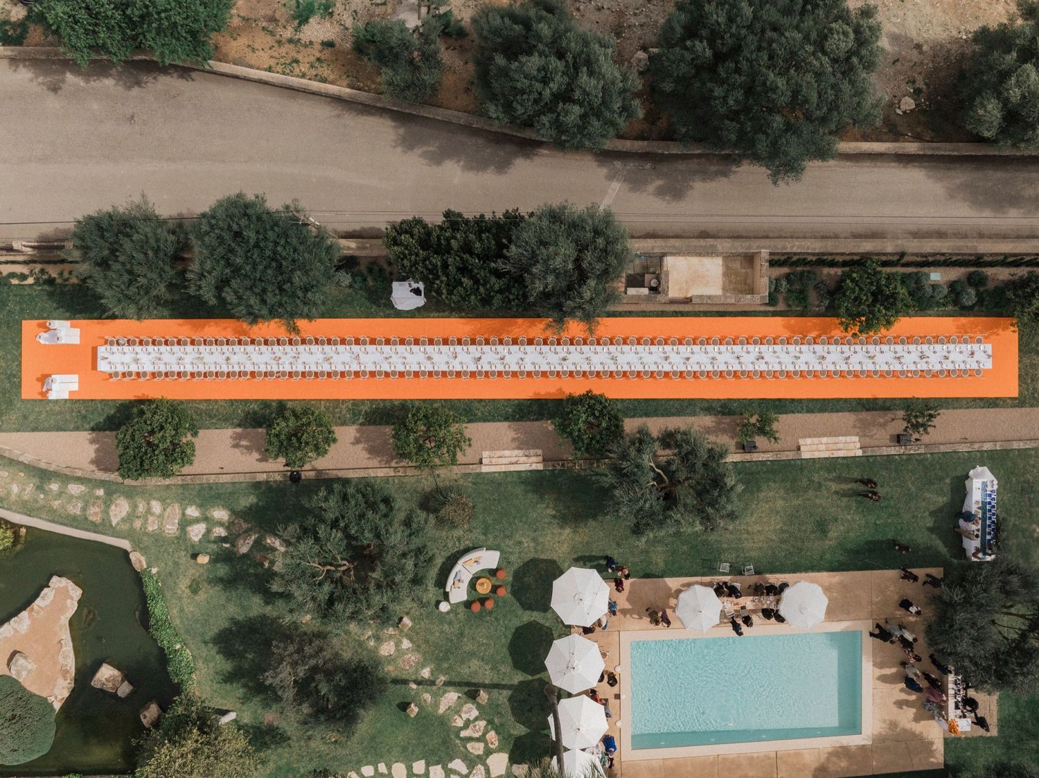 Aerial view of a backyard swimming pool surrounded by lush landscaping and outdoor furniture on a sunny day.