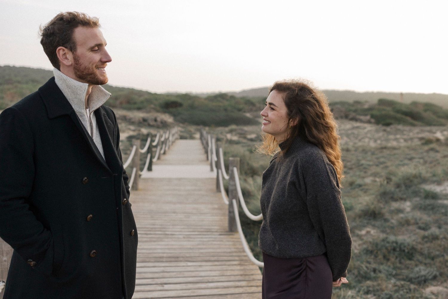 Couple walks together on wooden boardwalk through coastal dunes during golden hour.