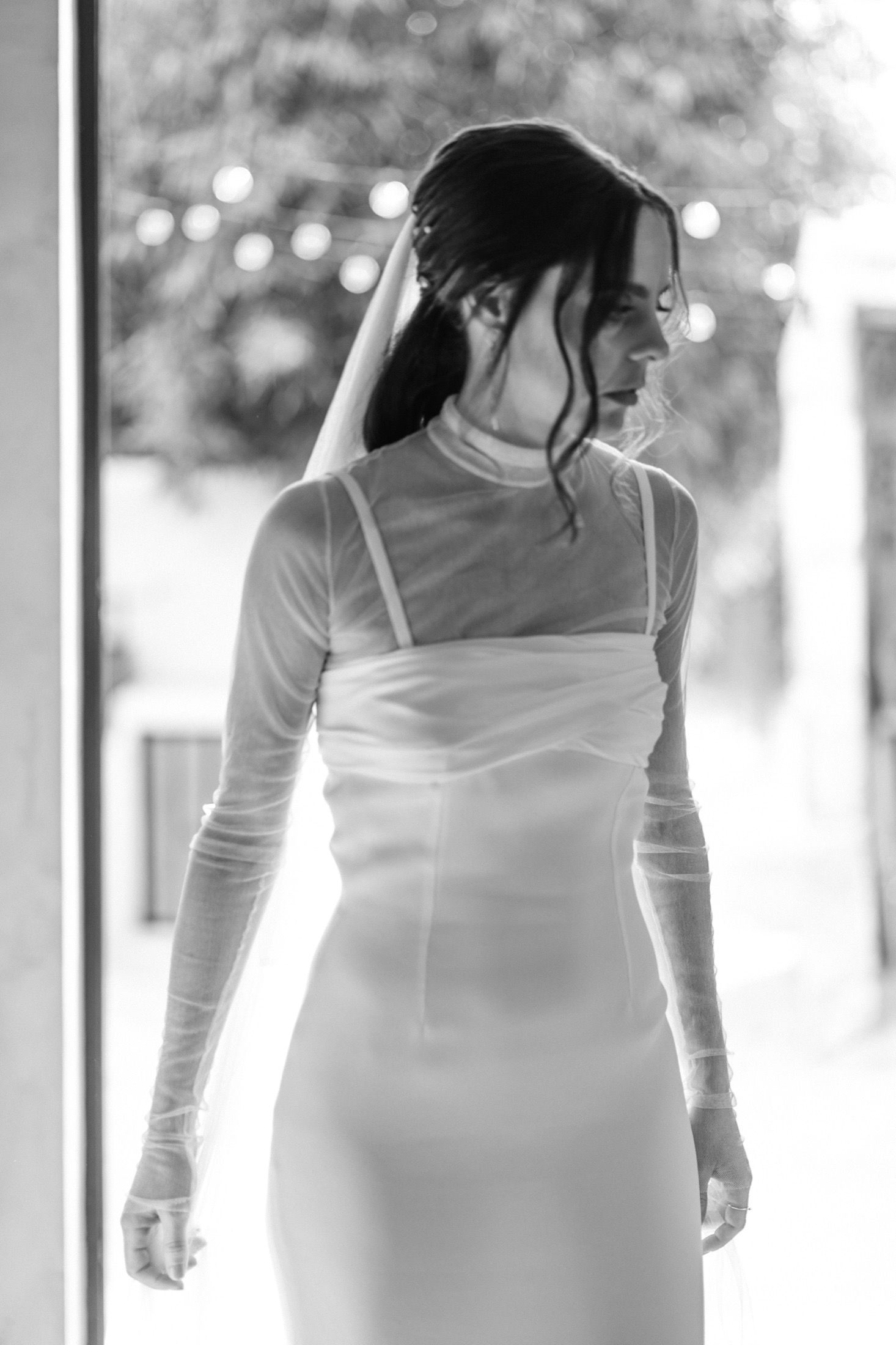 A person wearing a white dress stands in front of a window in a sequence of black and white photos.