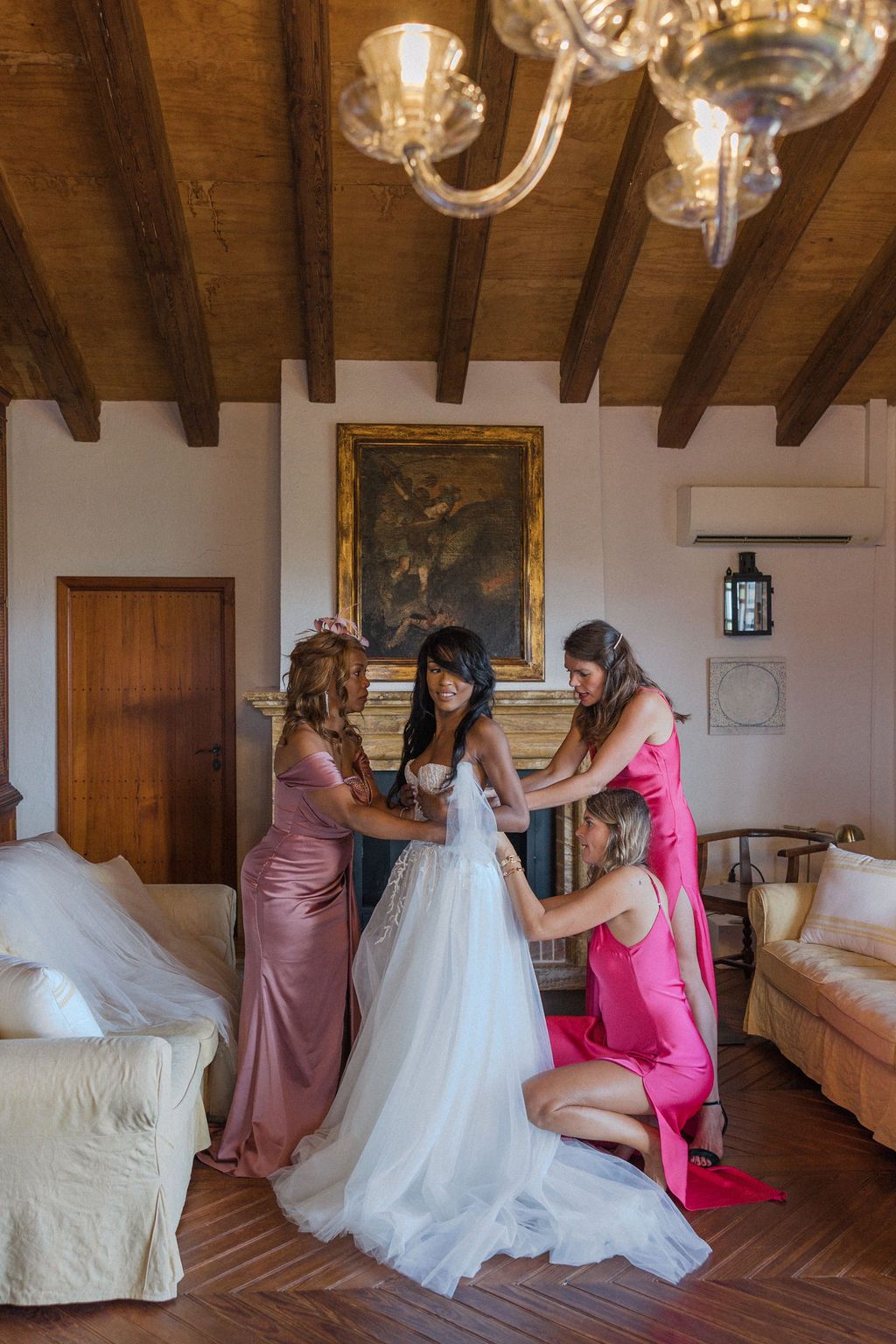 Wedding preparation scene with white dress and pink bridesmaid gowns in rustic room.