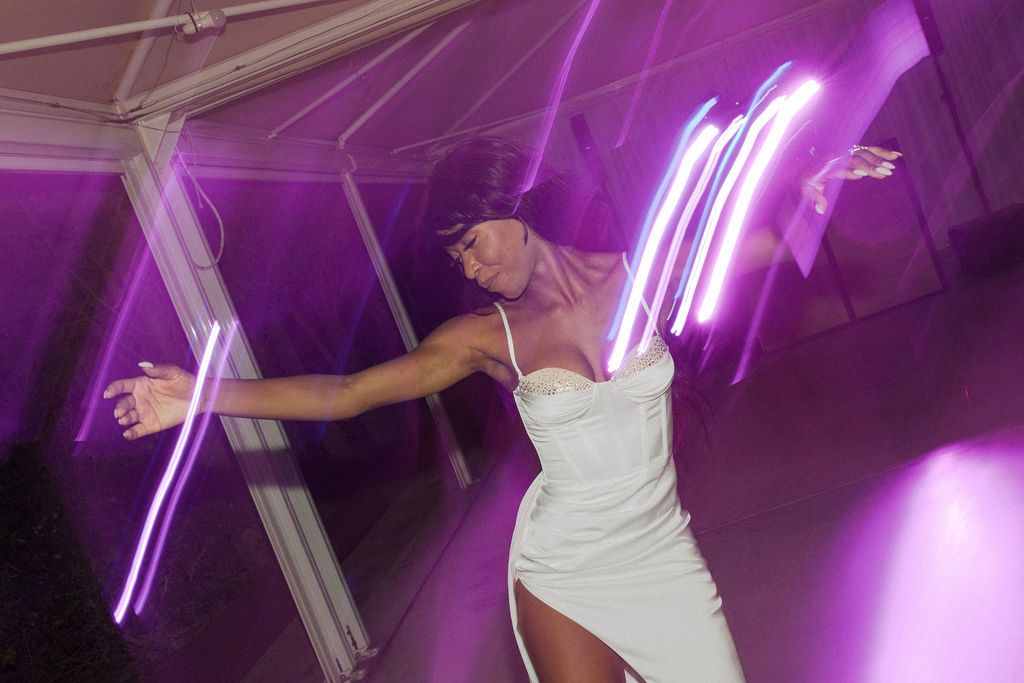 Dancers move under purple neon lighting in an indoor venue.