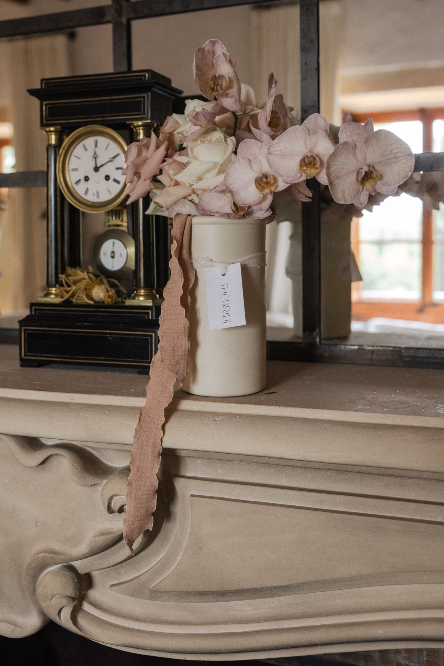 Vintage clocks and delicate pink flowers displayed on an ornate cream-colored mantelpiece.