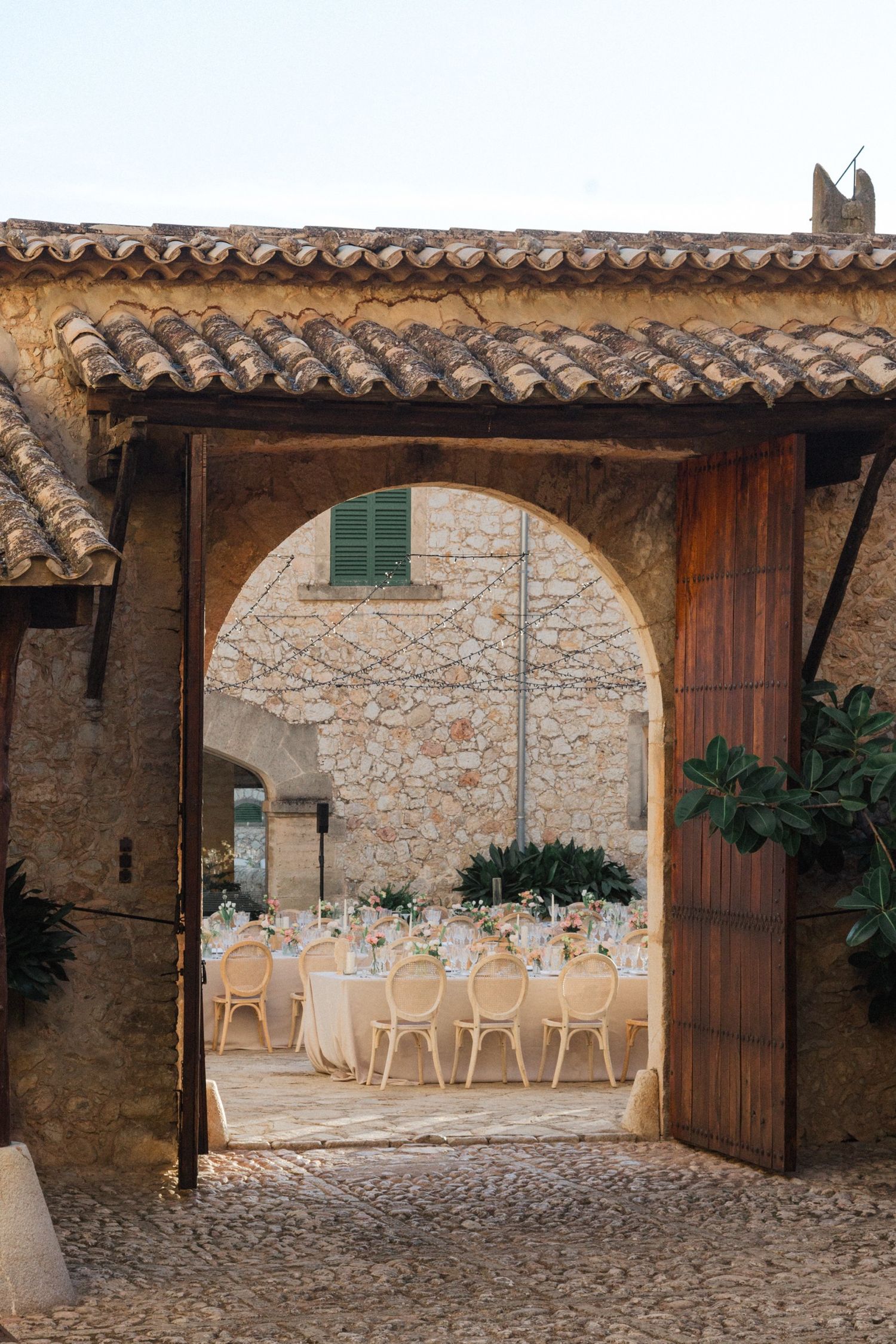 Stone archways and cobblestone courtyard of a rustic Mediterranean venue with wooden doors and dining setup.