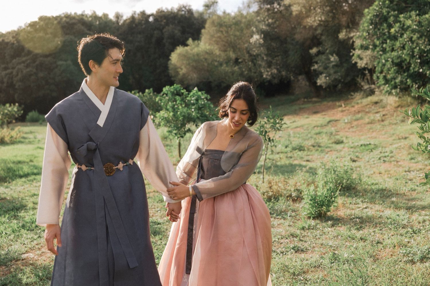 A couple walking together in a lush outdoor setting wearing casual attire and holding hands.