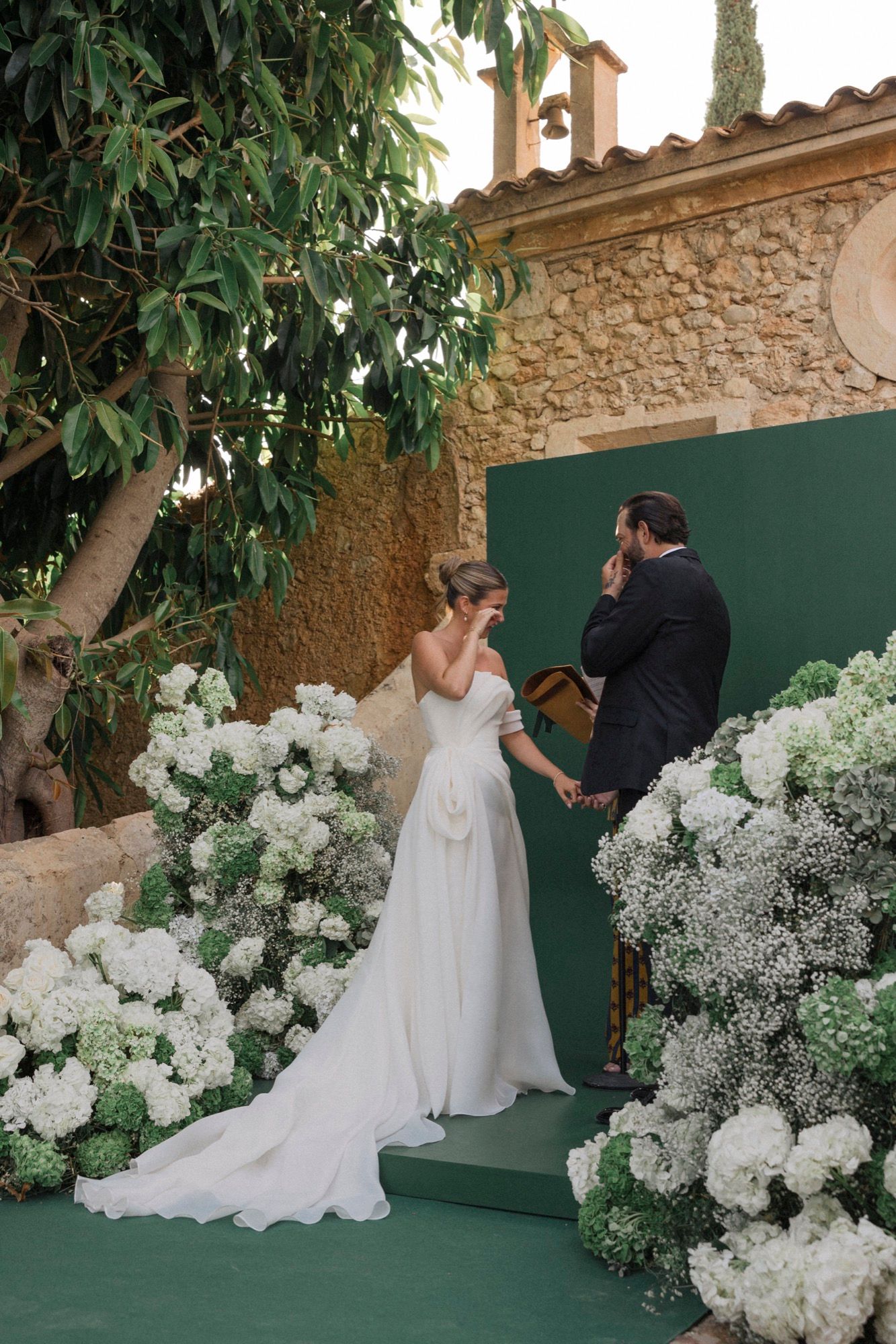 Elegant outdoor wedding ceremony with white hydrangeas and green backdrop against stone architecture.