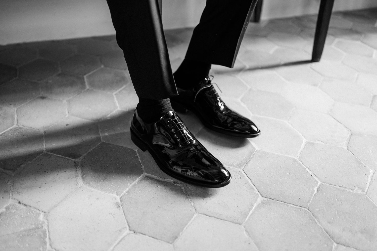 Close-up view of formal black dress shoes on a tiled floor at a wedding.