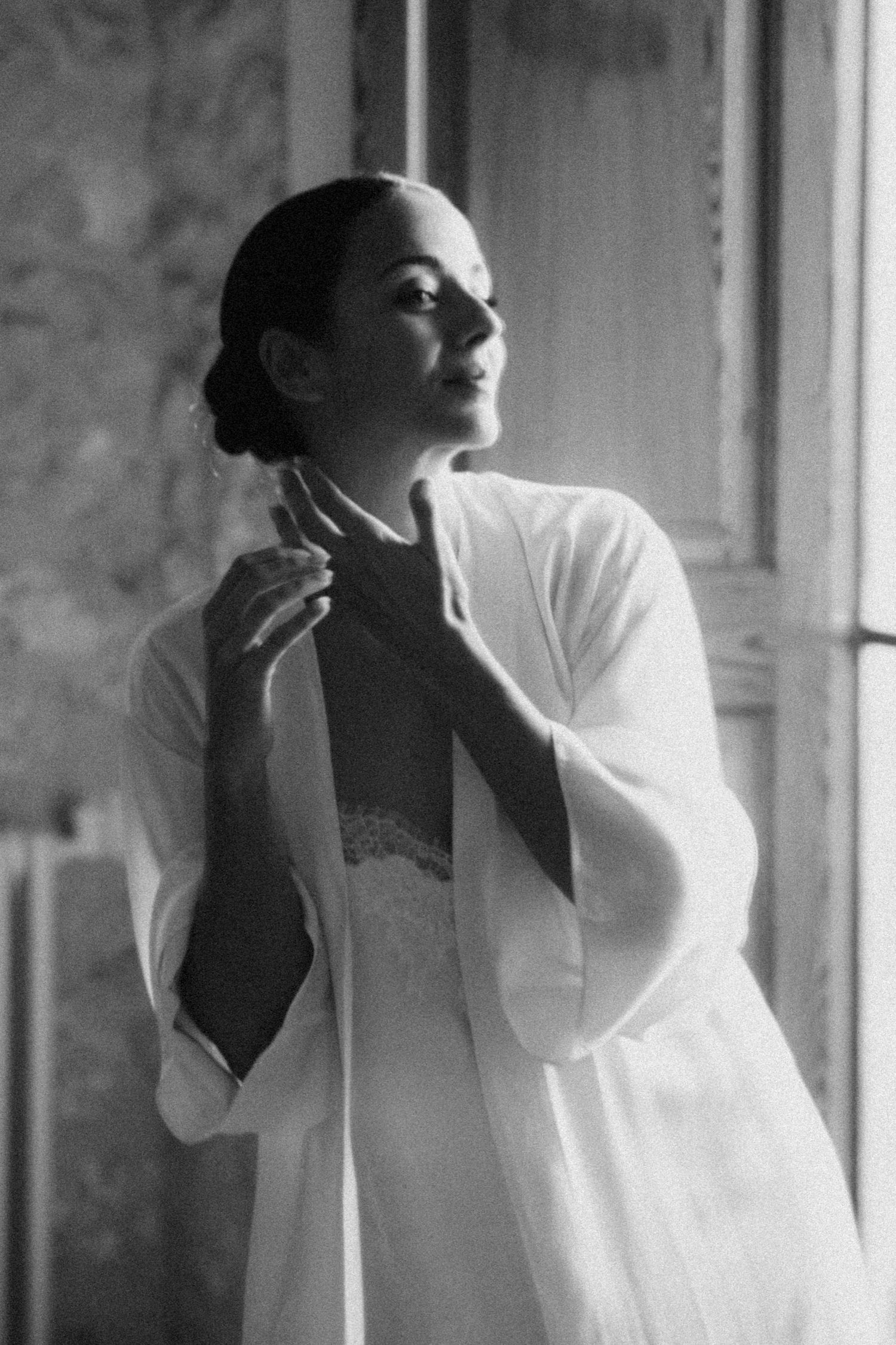 Figure in flowing white garment poses gracefully against textured wall.