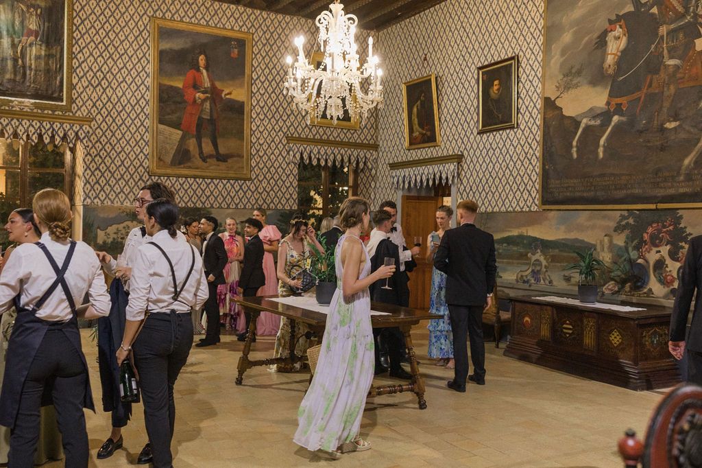 Elegant reception hall with chandeliers and historical artwork on wallpapered walls.