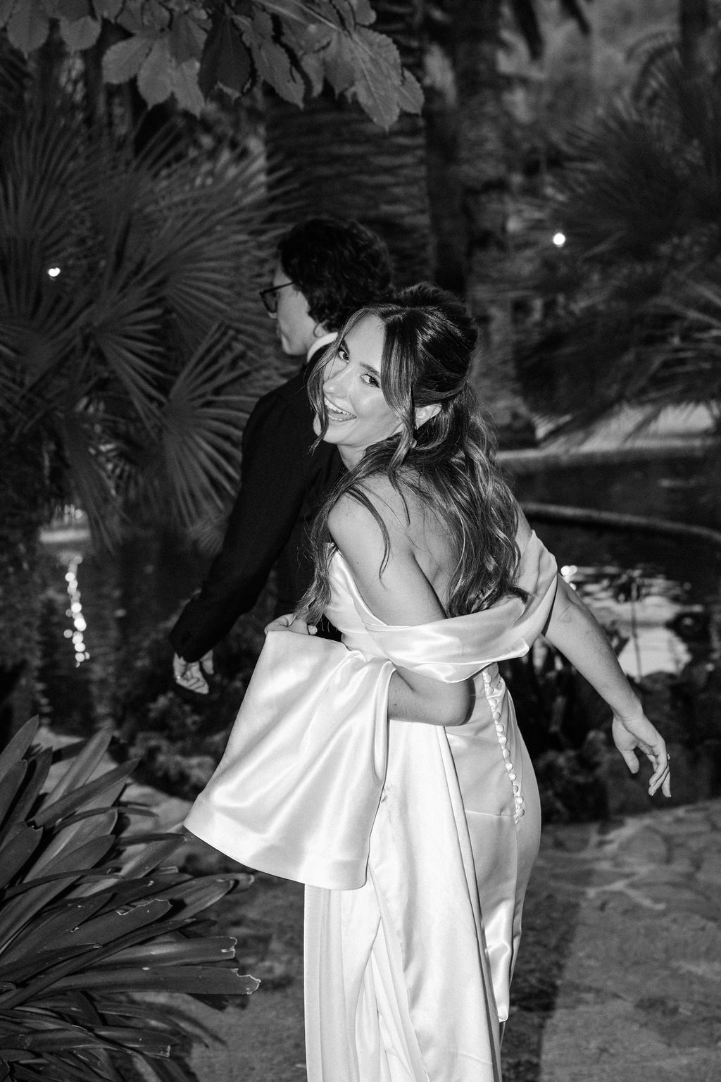 Black and white photo of couple dancing outdoors among palm trees at night.