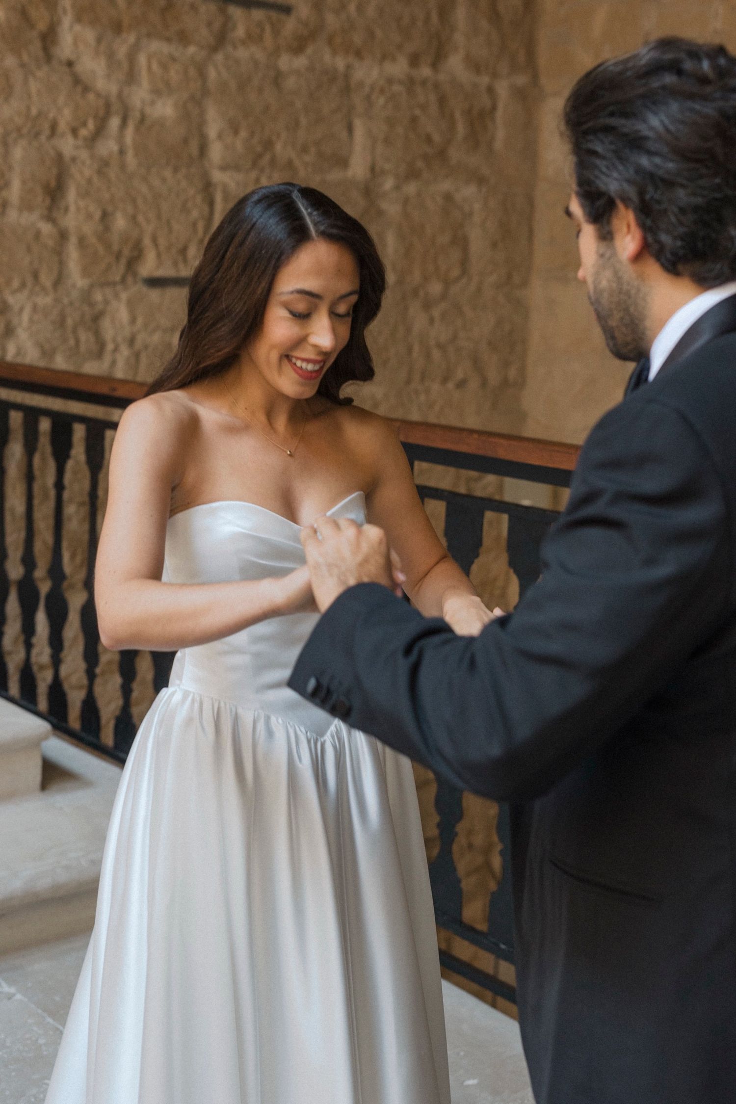 A couple shares a tender moment in a stone hallway, with the bride wearing a flowing white dress and groom in dark suit.