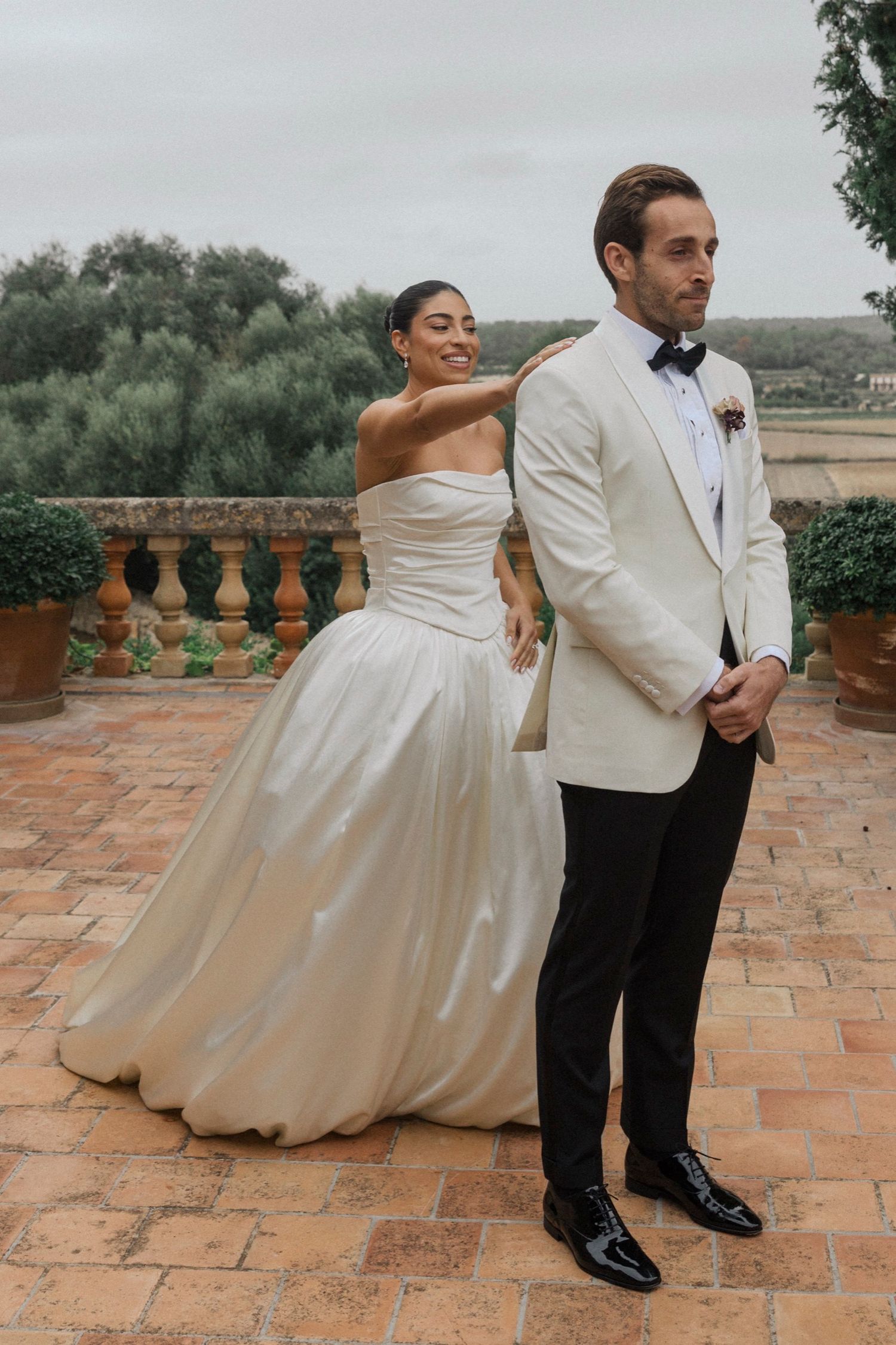 Wedding couple poses creatively on terrace with bride dipping backwards in flowing white gown and groom in tuxedo.