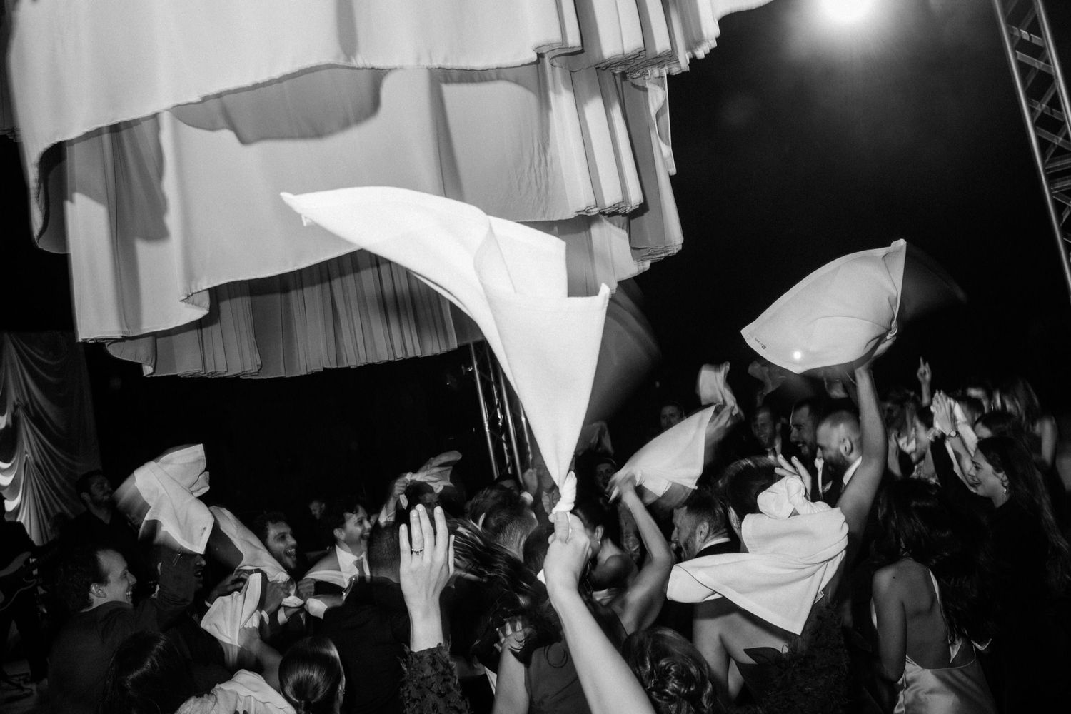 A crowd of concert-goers wave white flags during an energetic black and white performance shot.