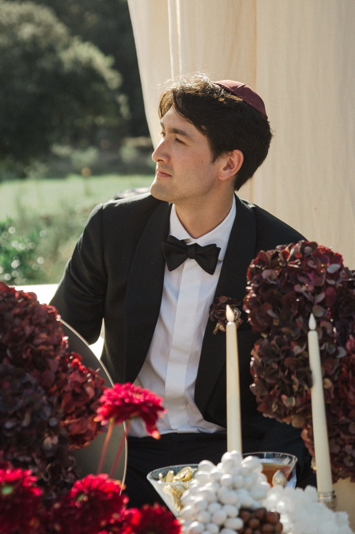 Elegant formal table setting with deep red floral arrangements and white candles at an outdoor wedding reception.