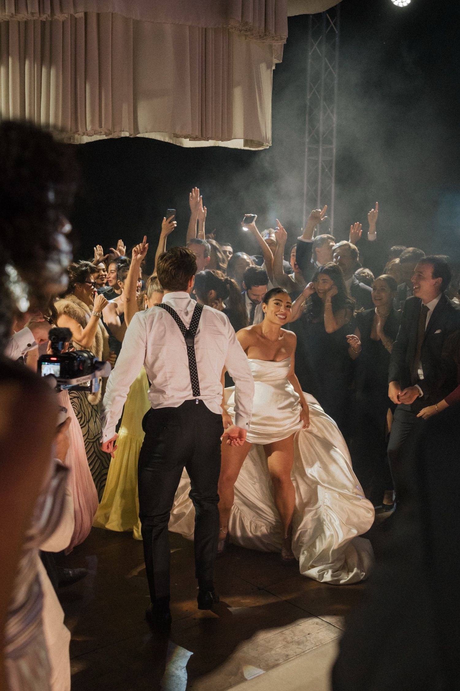 A lively wedding reception dance floor filled with guests celebrating under dramatic lighting.