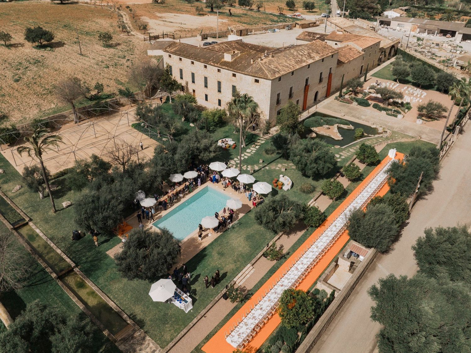 Aerial view of a Spanish villa with orange and white striped awning and swimming pool in Mediterranean landscape.