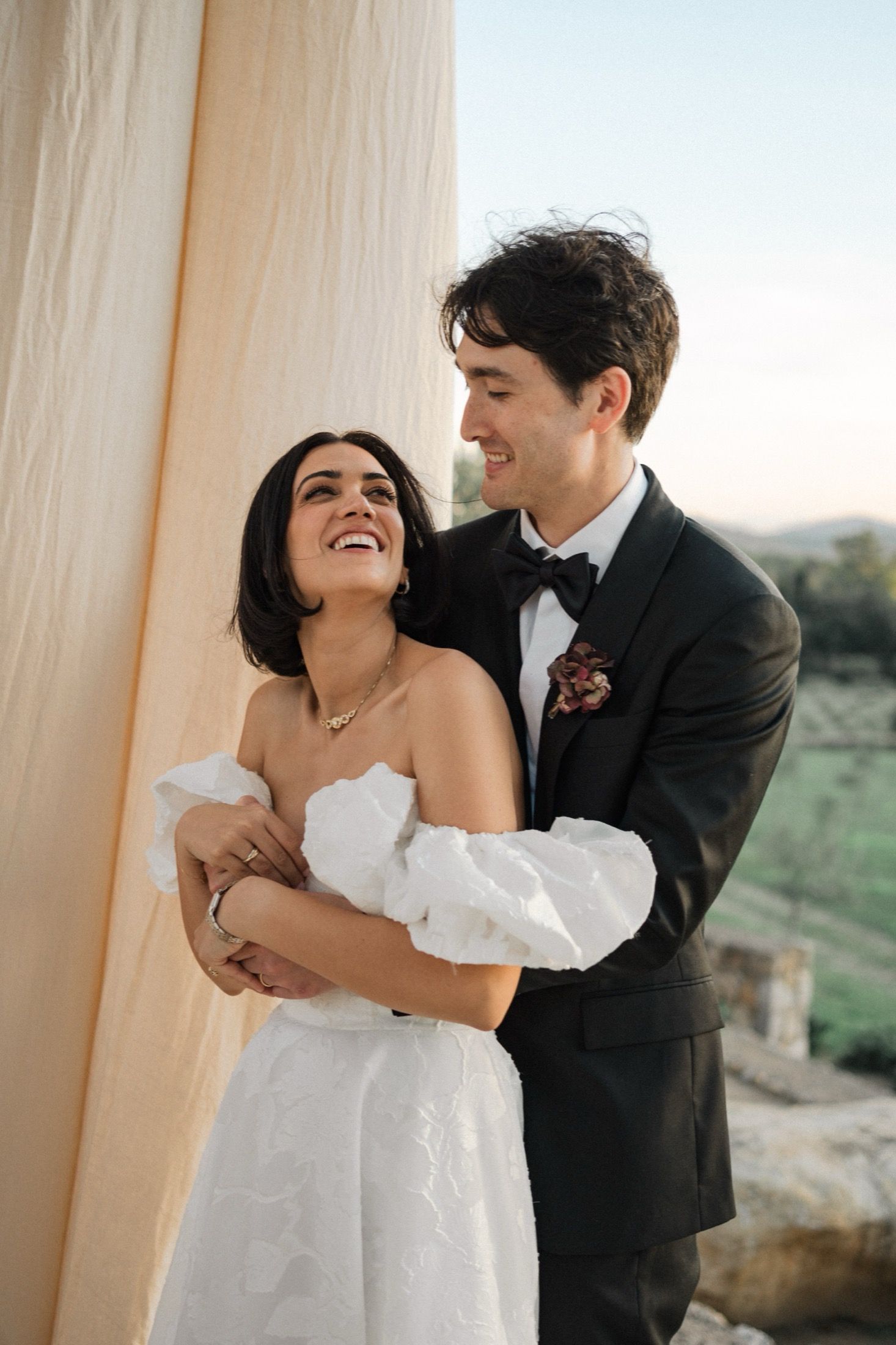 A happy couple shares a joyful moment together on their wedding day, wearing traditional formal attire.