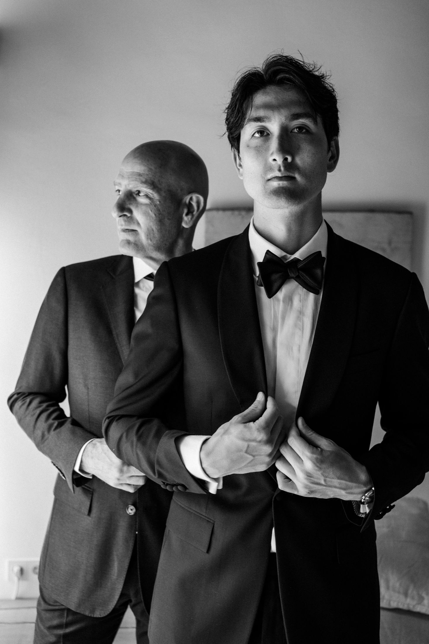 Black and white photo series showing figures in dark suits making dramatic gestures against a plain wall.