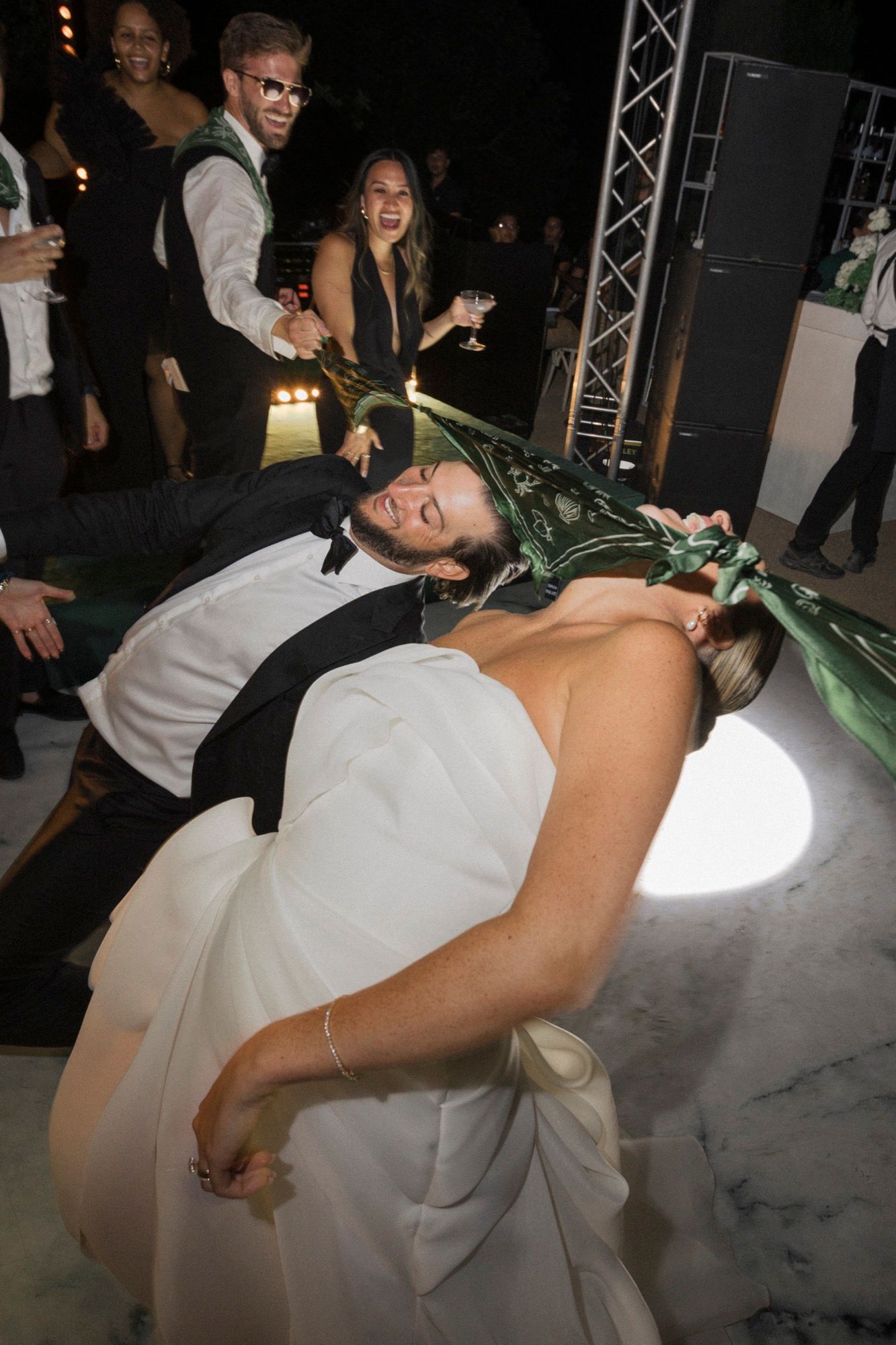 Wedding couple shares playful moment on dance floor with guests during reception.