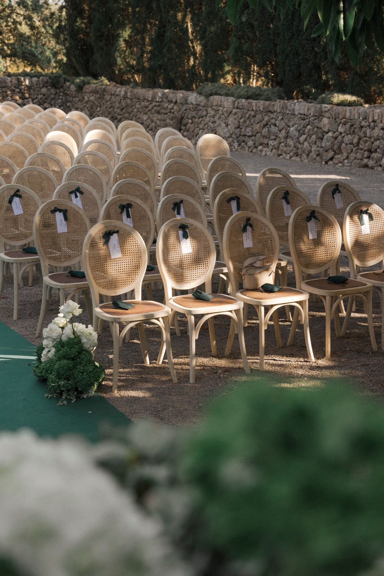 Elegant wedding chairs lined up with white floral arrangements along a green carpet aisle.