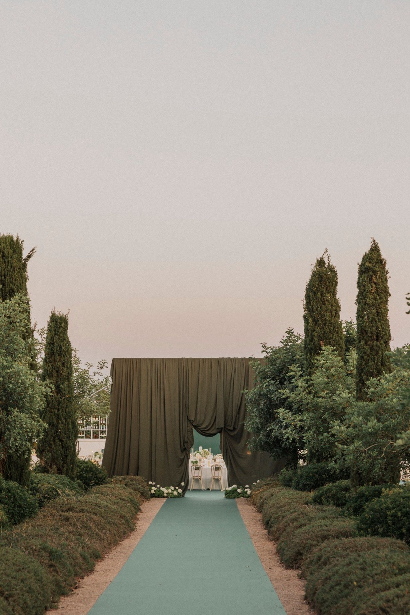 Outdoor wedding venue setup with tall cypress trees and dark draping creating an intimate space.