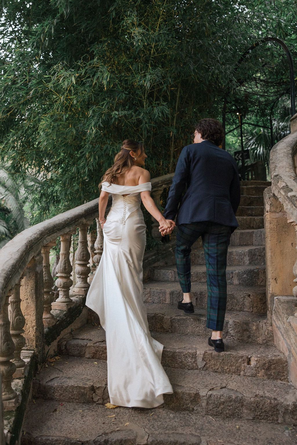 Wedding couple descends stone steps surrounded by lush garden foliage.