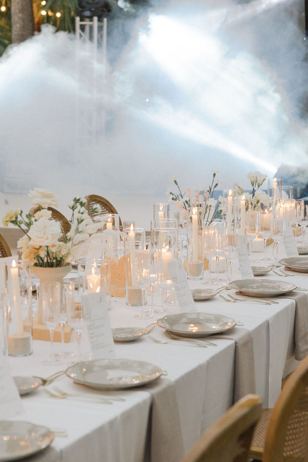 Elegant table settings with glowing candles and white decor for outdoor wedding reception.