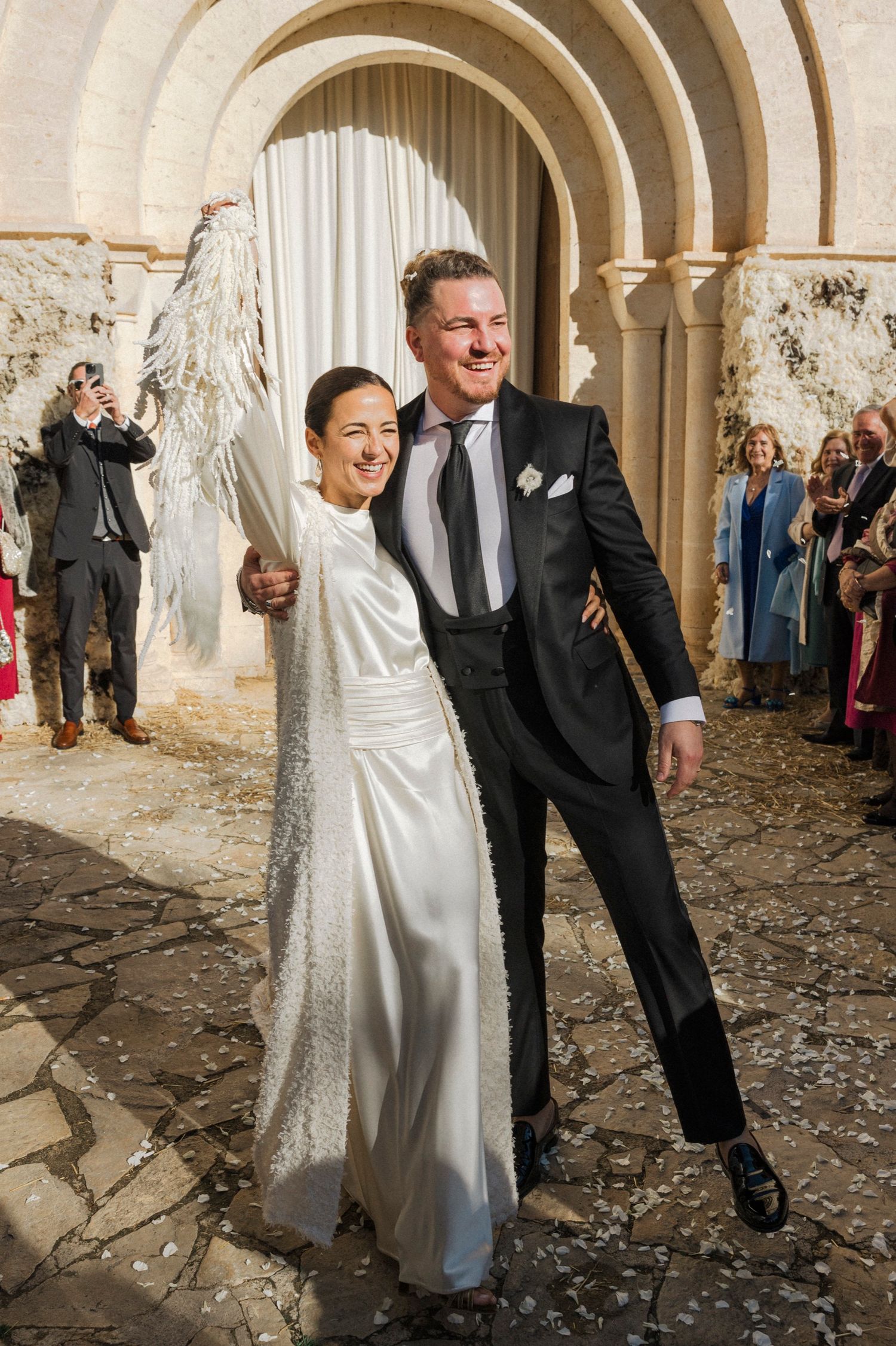 Happy couple celebrating under stone arches with confetti falling around them.