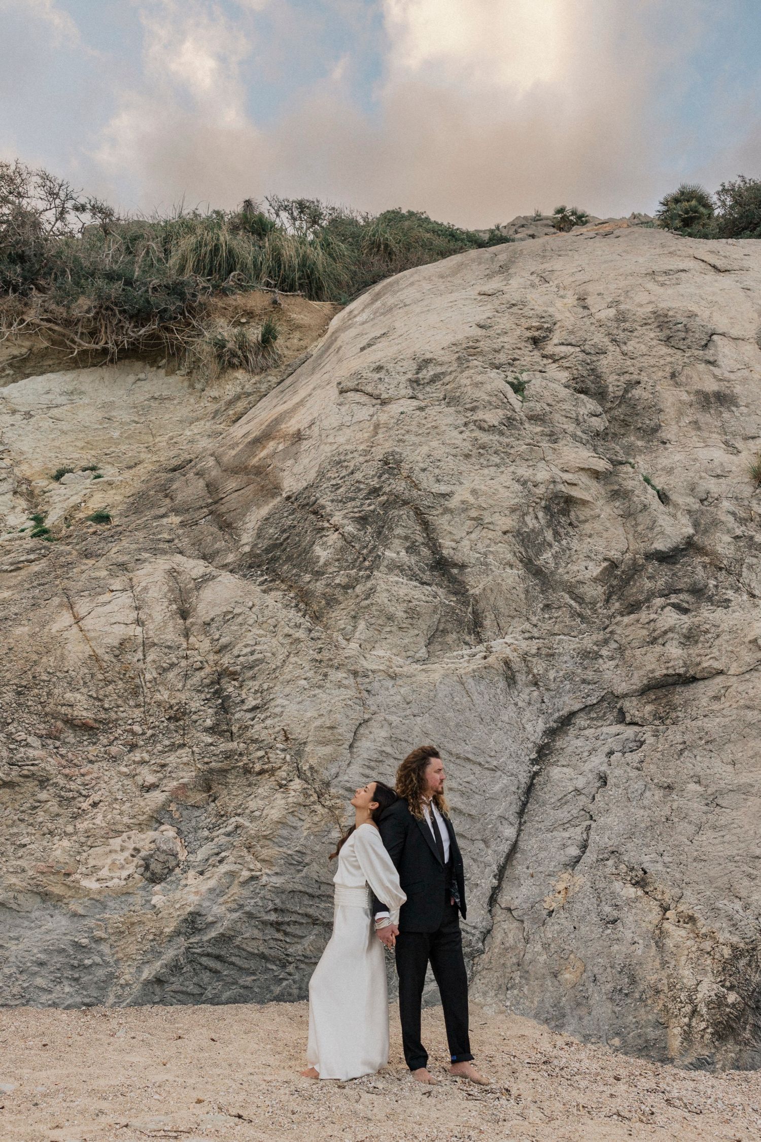 Couple in contrasting black and white outfits pose against dramatic rocky landscape.