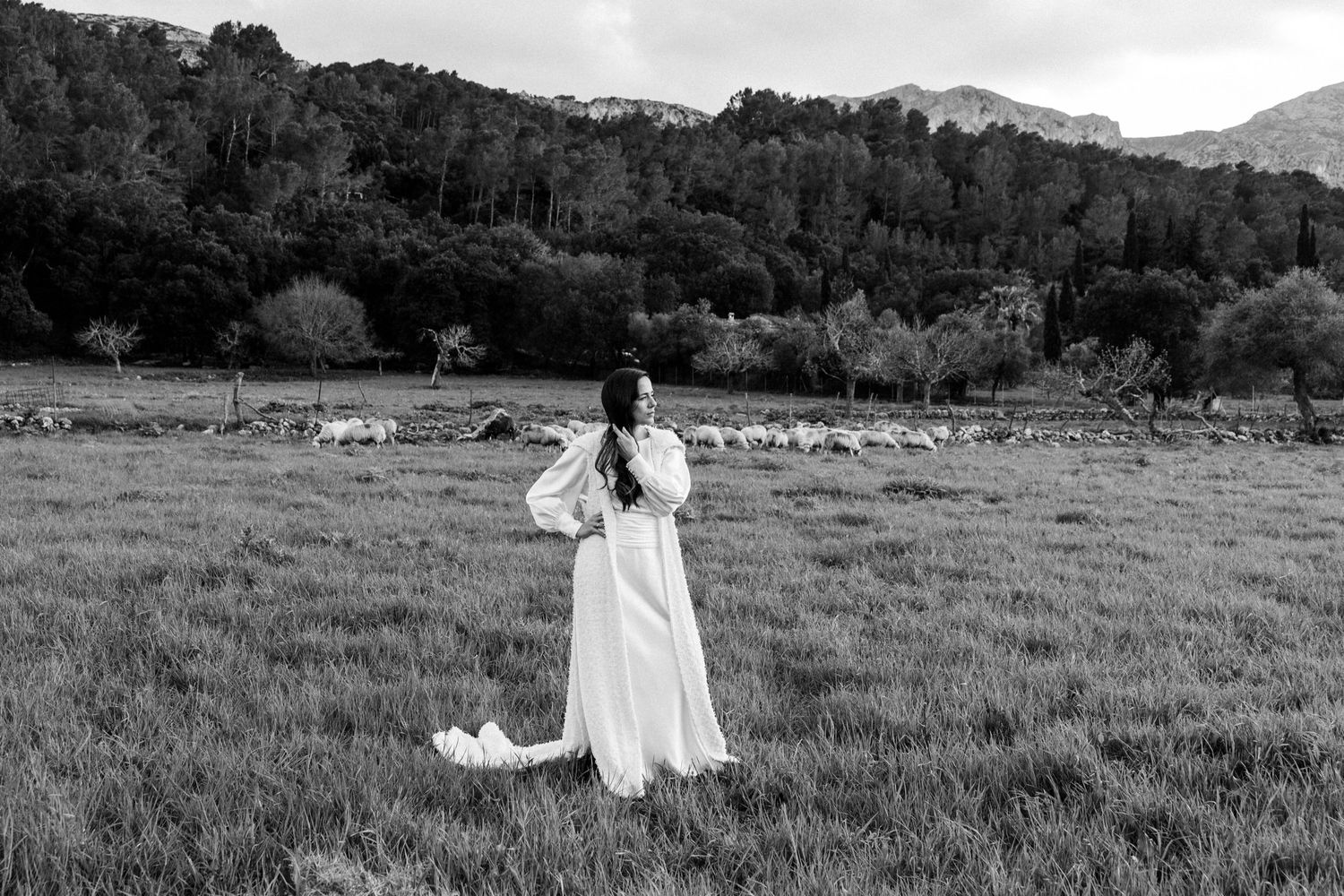 Black and white landscape with figure spinning in meadow against mountain backdrop.