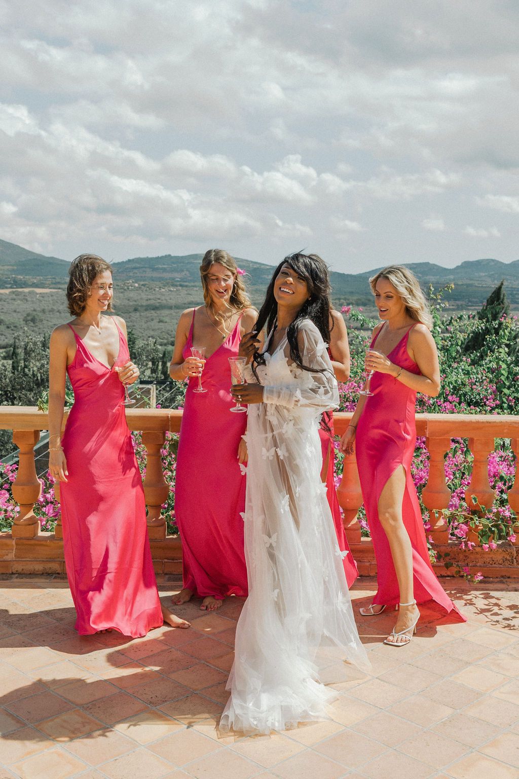 Bridesmaids in bright pink dresses pose on a terrace overlooking scenic mountain views.