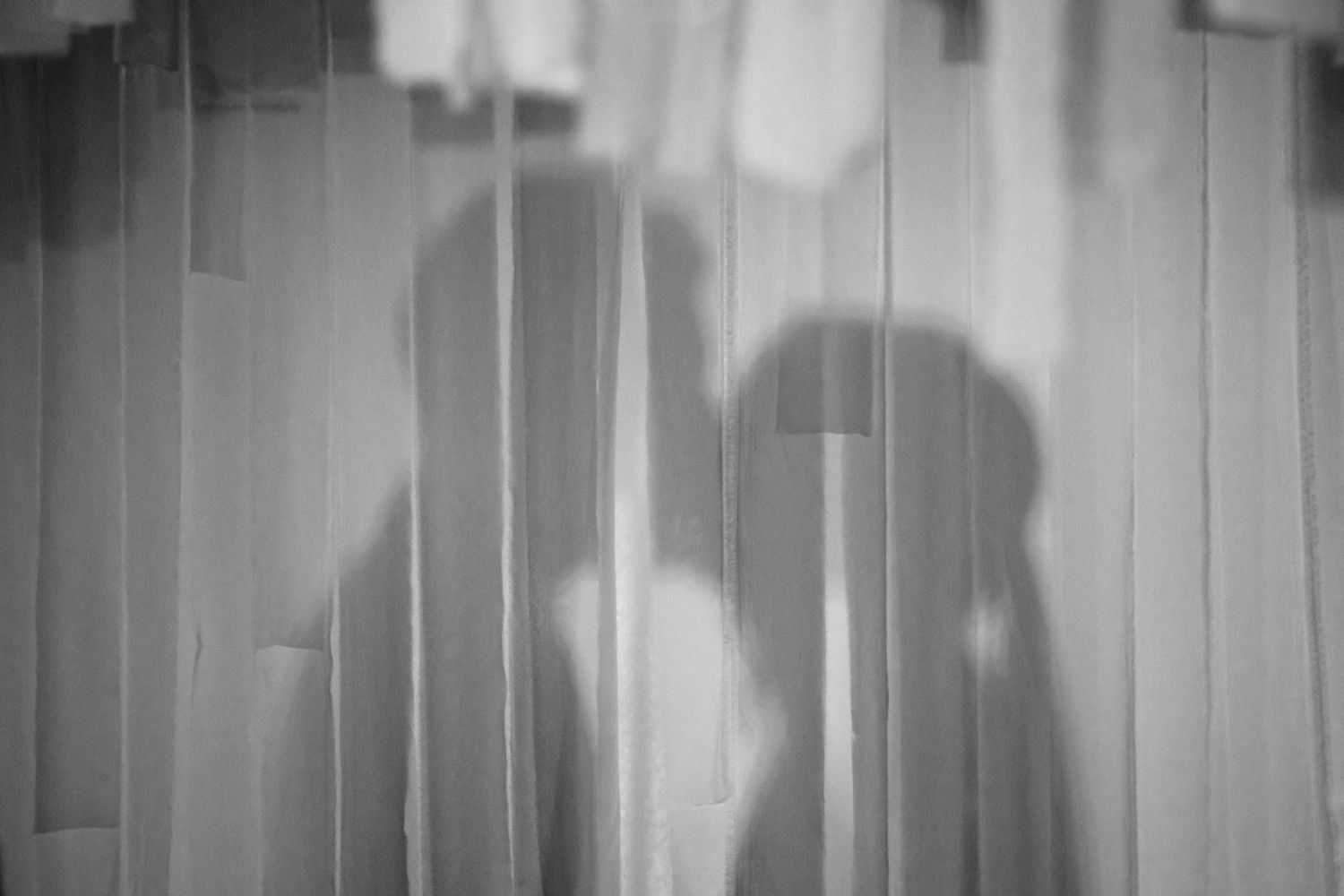 A black and white photograph shows a row of people silhouetted against a bright background with vertical lines.