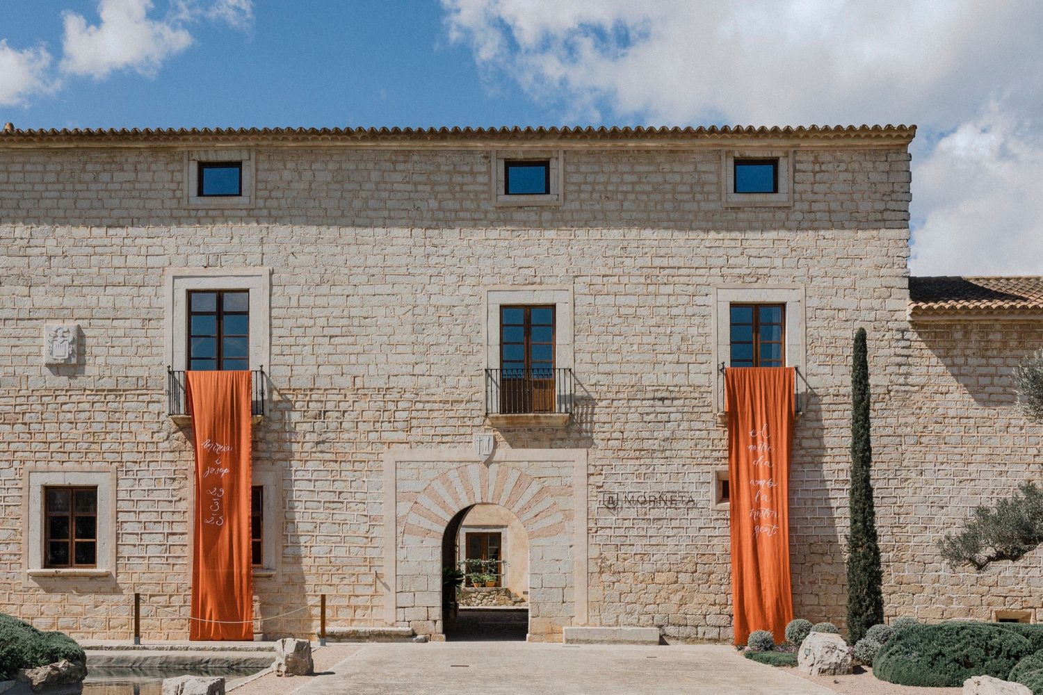 Historic stone building facade with two large orange banners hanging on either side of a central archway entrance.
