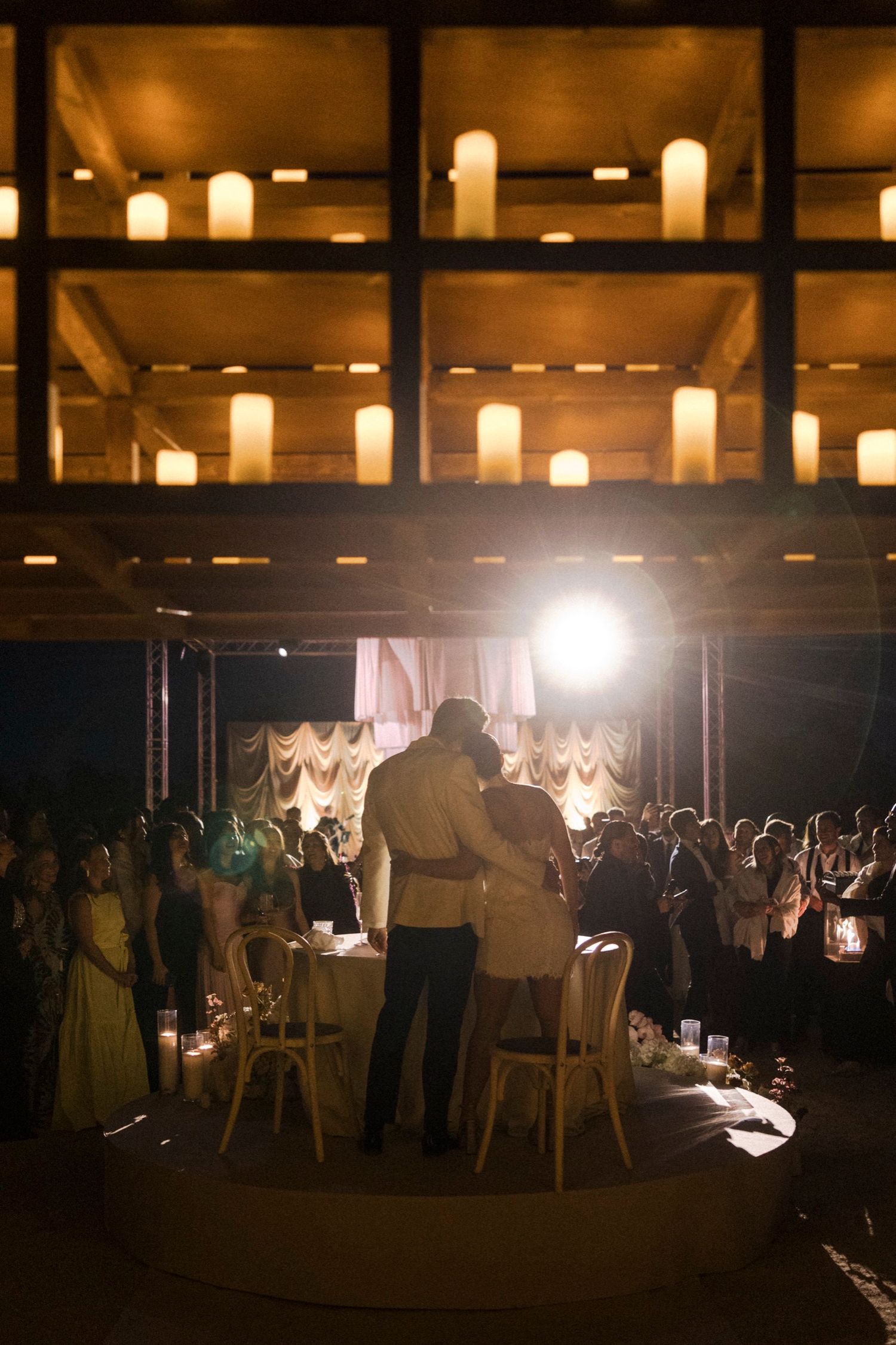 A romantic wedding reception scene with glowing candles overhead and a couple standing on a circular stage surrounded by guests.