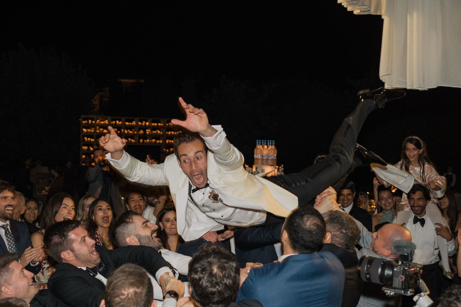 A crowd lifts and carries someone during a lively celebration at an evening event.