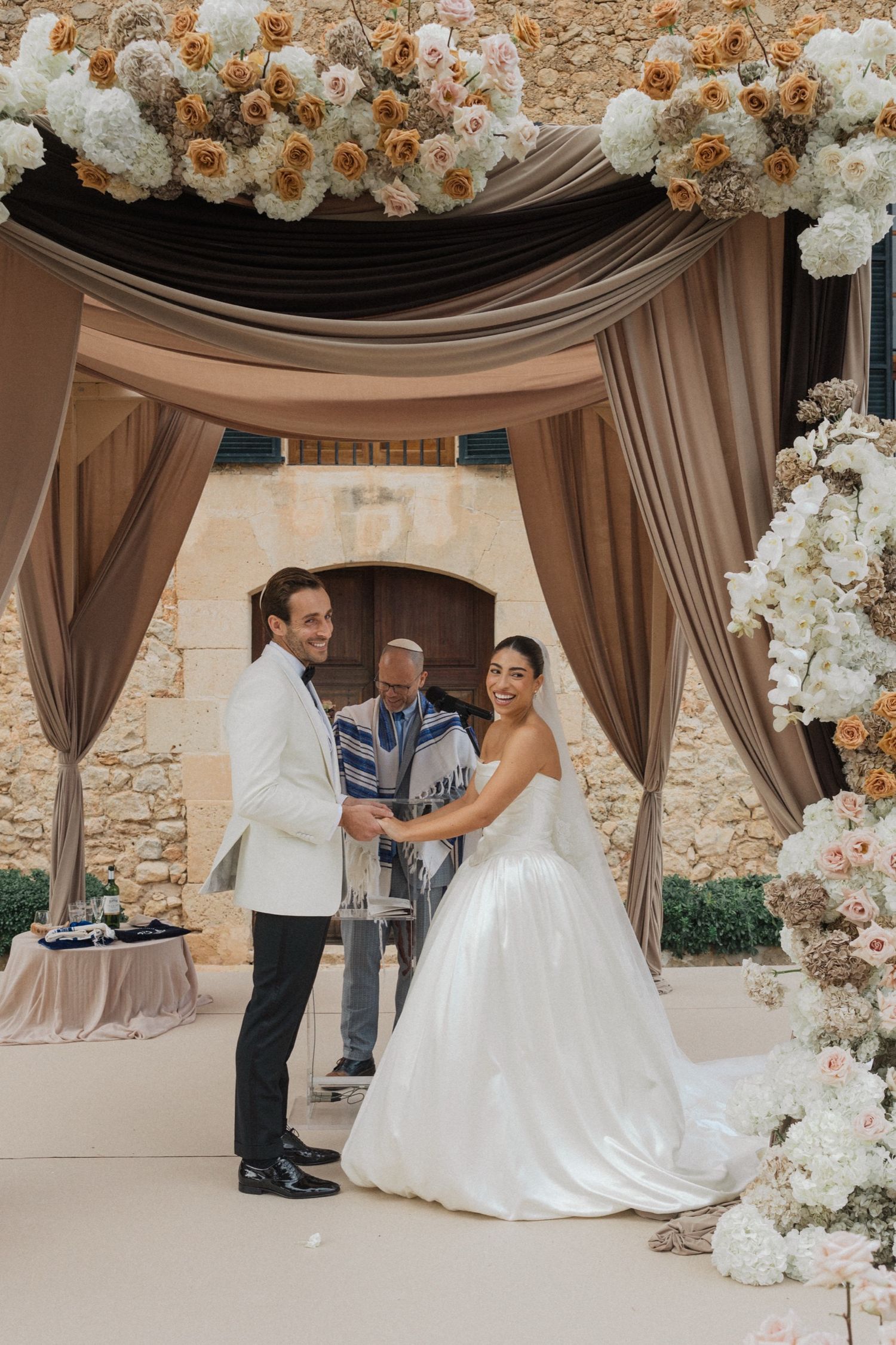 Wedding ceremony under an elegant floral arch with draped fabric and white flower decorations.