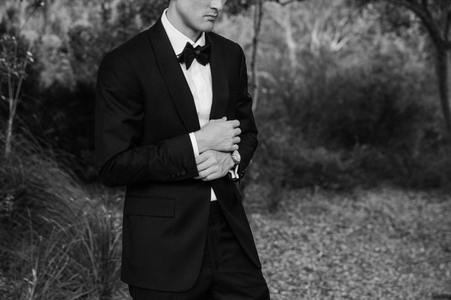A black and white photo collage showing seven poses of a person in a tuxedo standing outdoors.