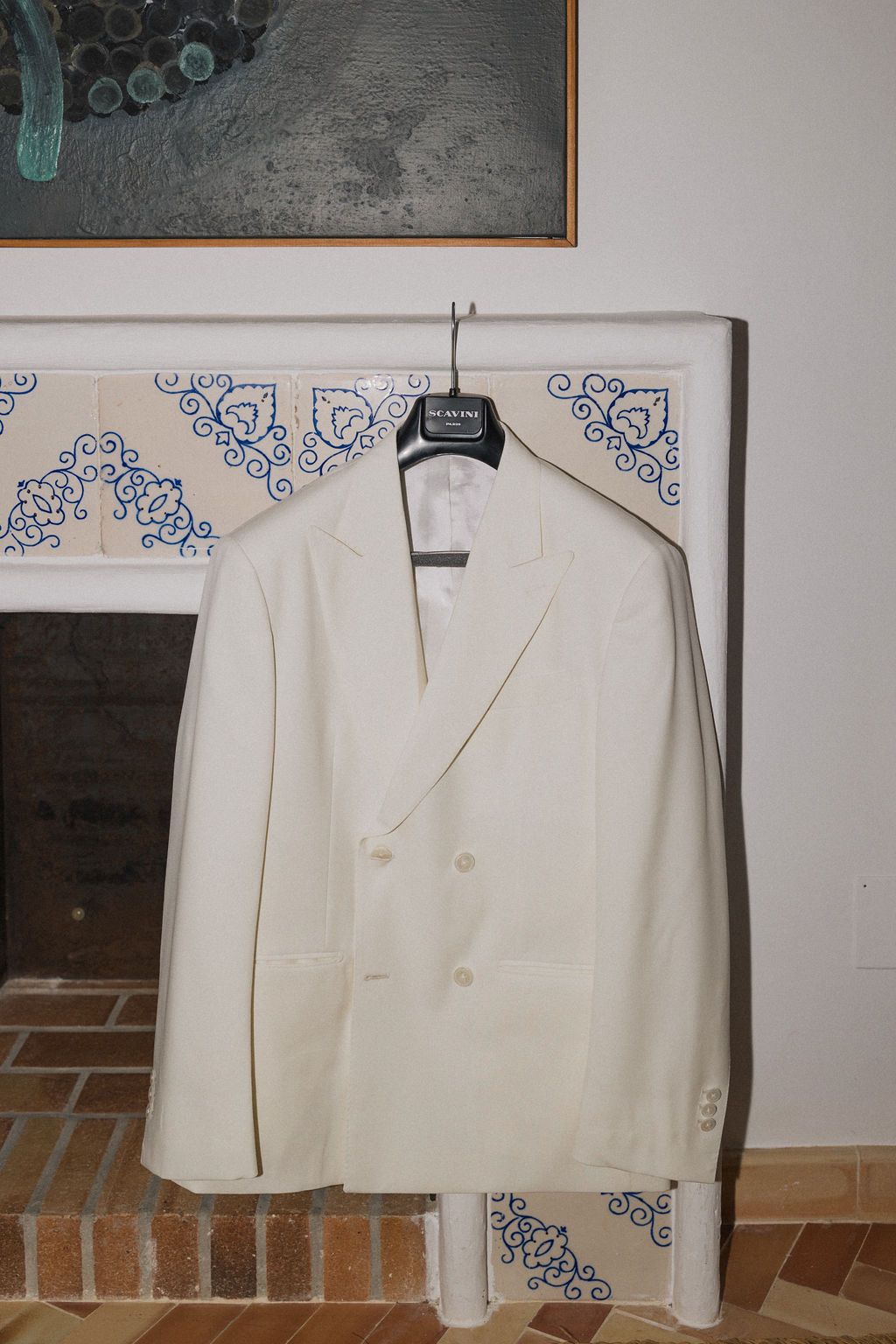 A white formal dinner jacket displayed on a hanger against a wall with decorative blue corner designs.