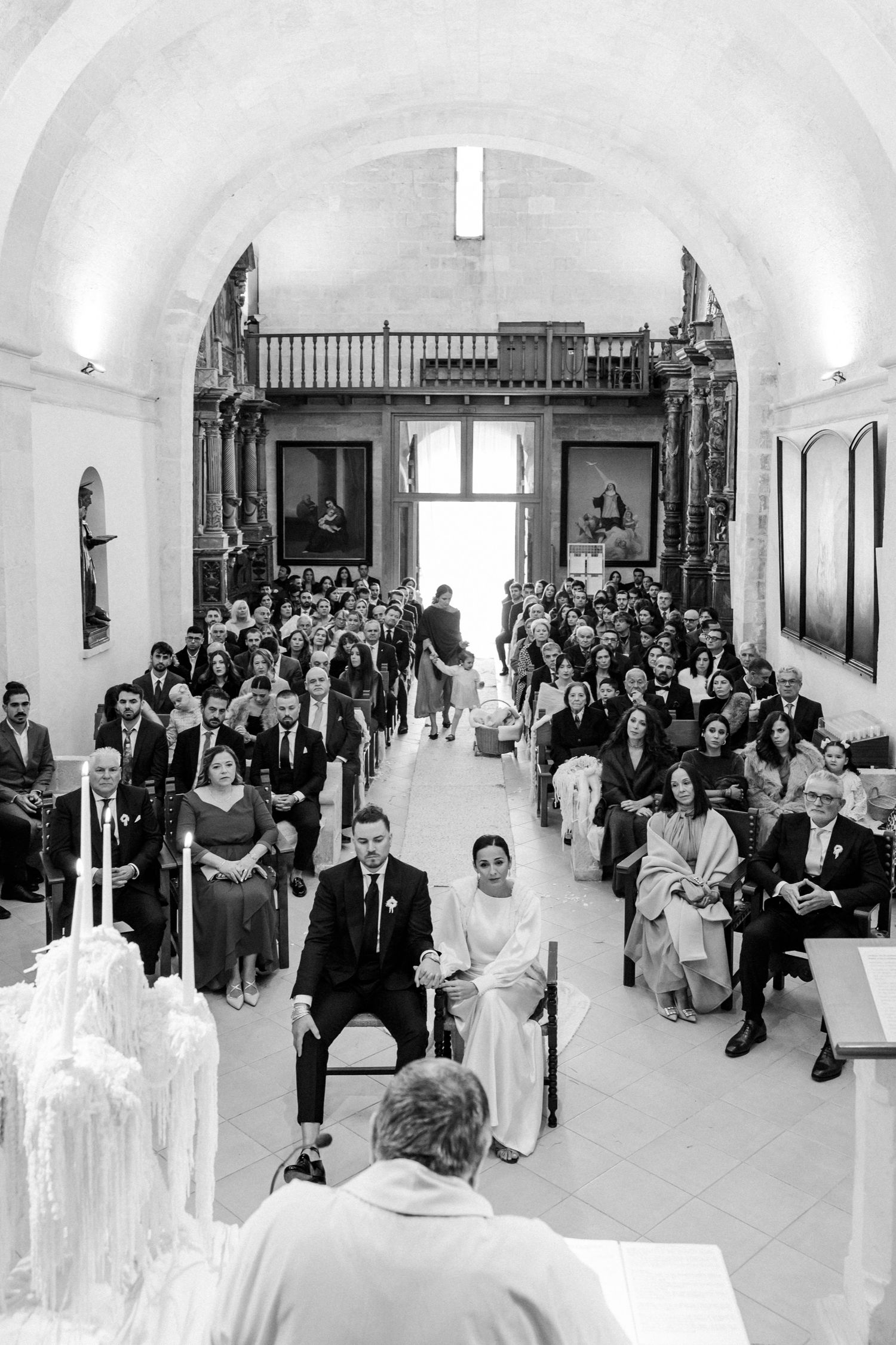 Wide view of wedding guests seated in church pews during ceremony.
