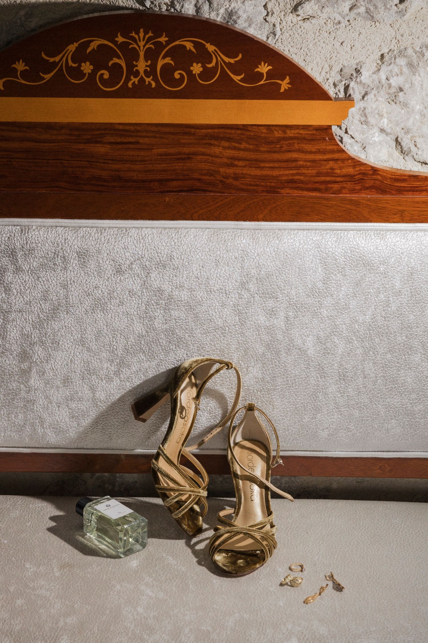 Gold high heel shoes and jewelry arranged on textured gray surface against wooden backdrop.
