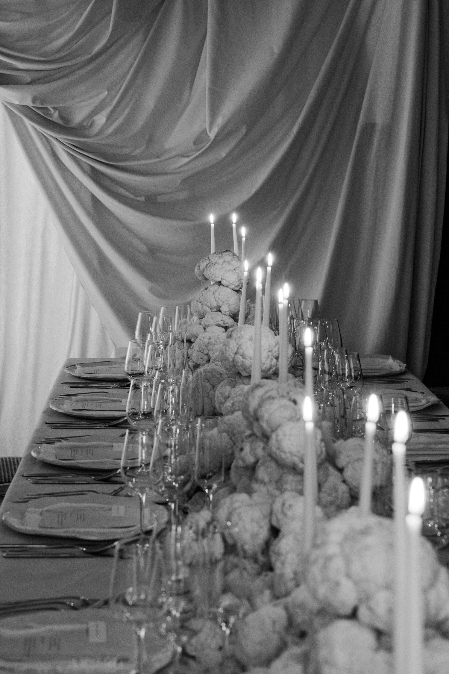 Black and white photo of an elegant table setting with white flowers and glowing candles.
