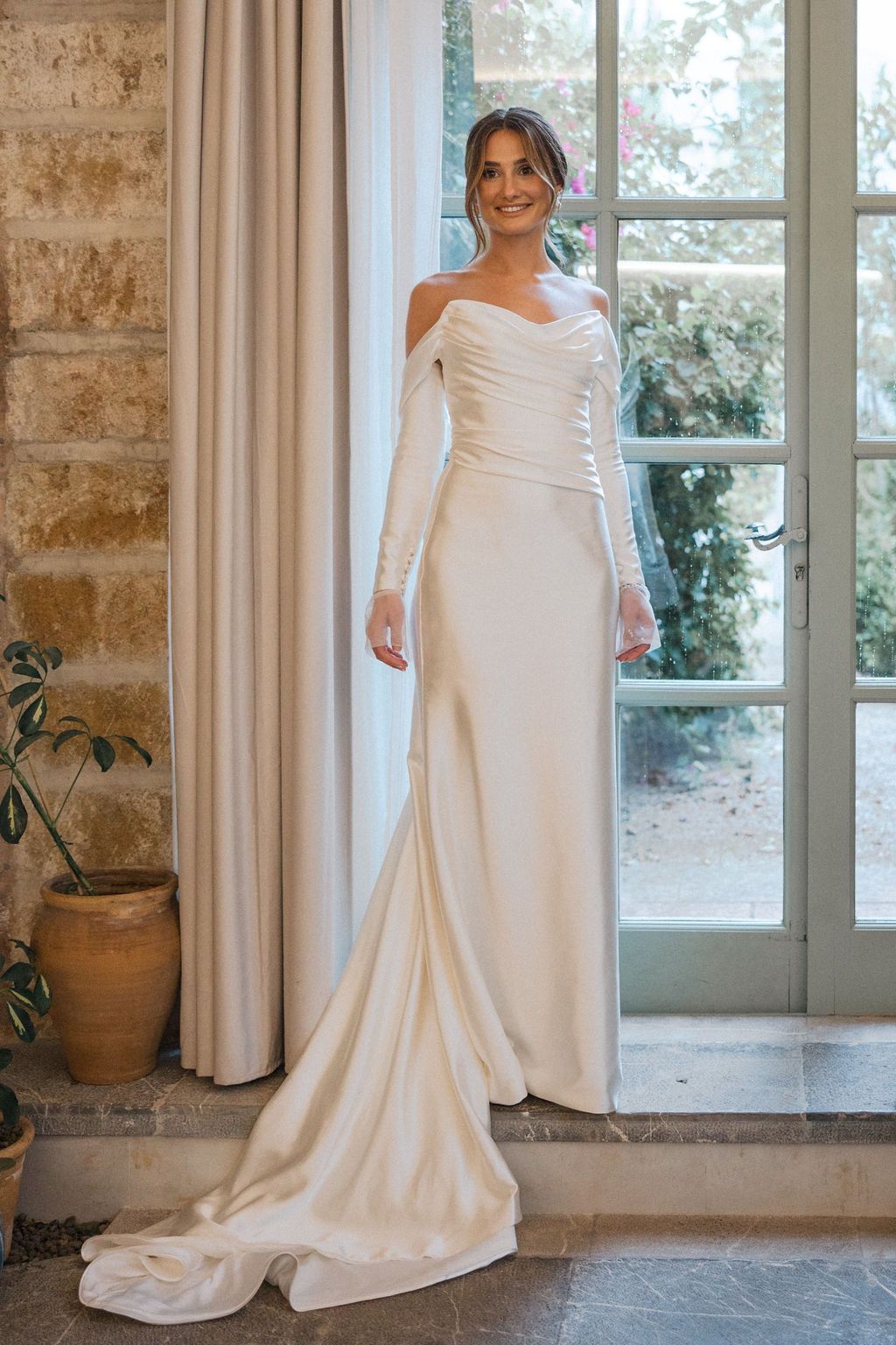 Elegant white wedding dress with flowing train displayed in a rustic room with French doors.