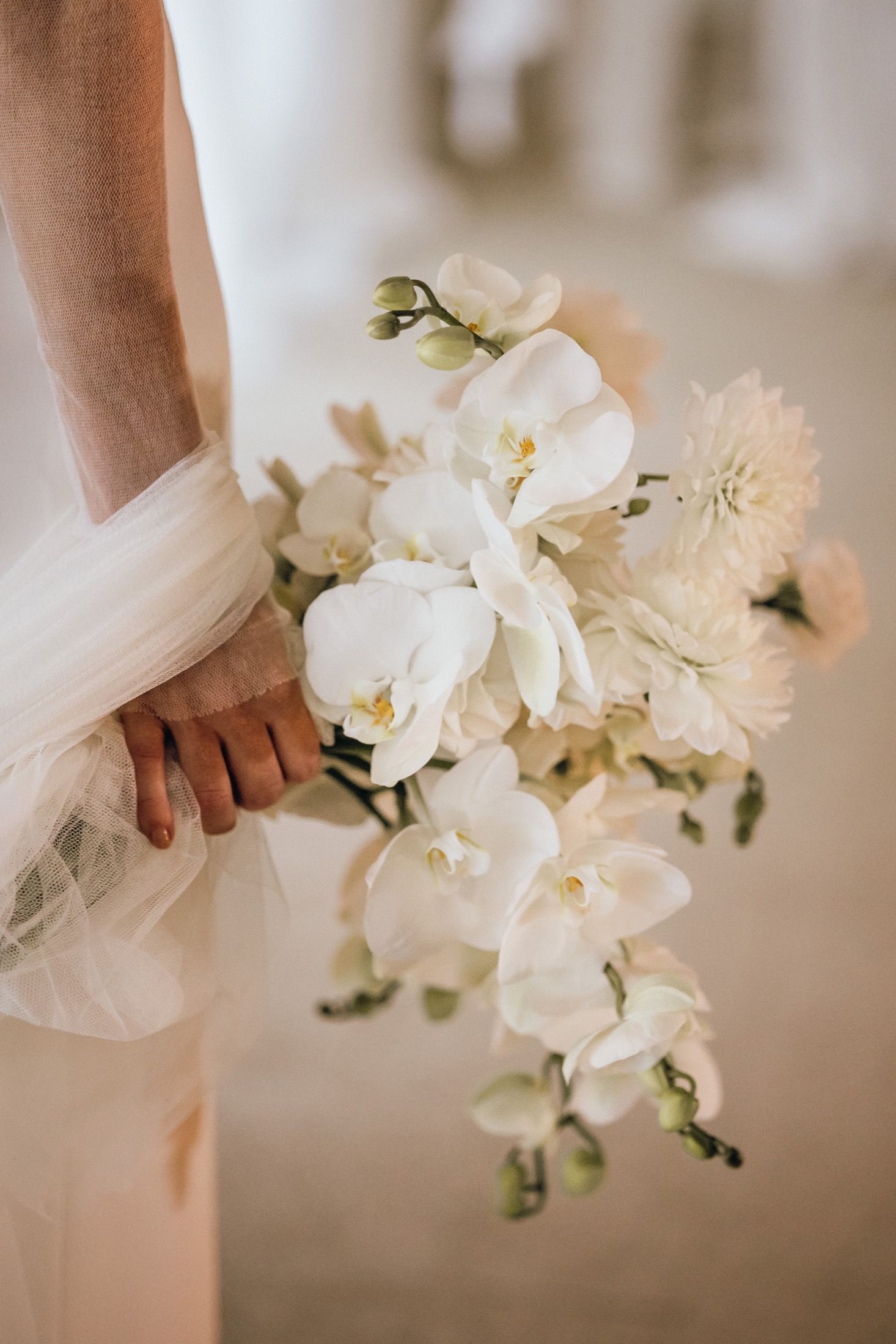 A delicate cascade of white orchids and flowers adorns a wedding bouquet held against soft tulle fabric.