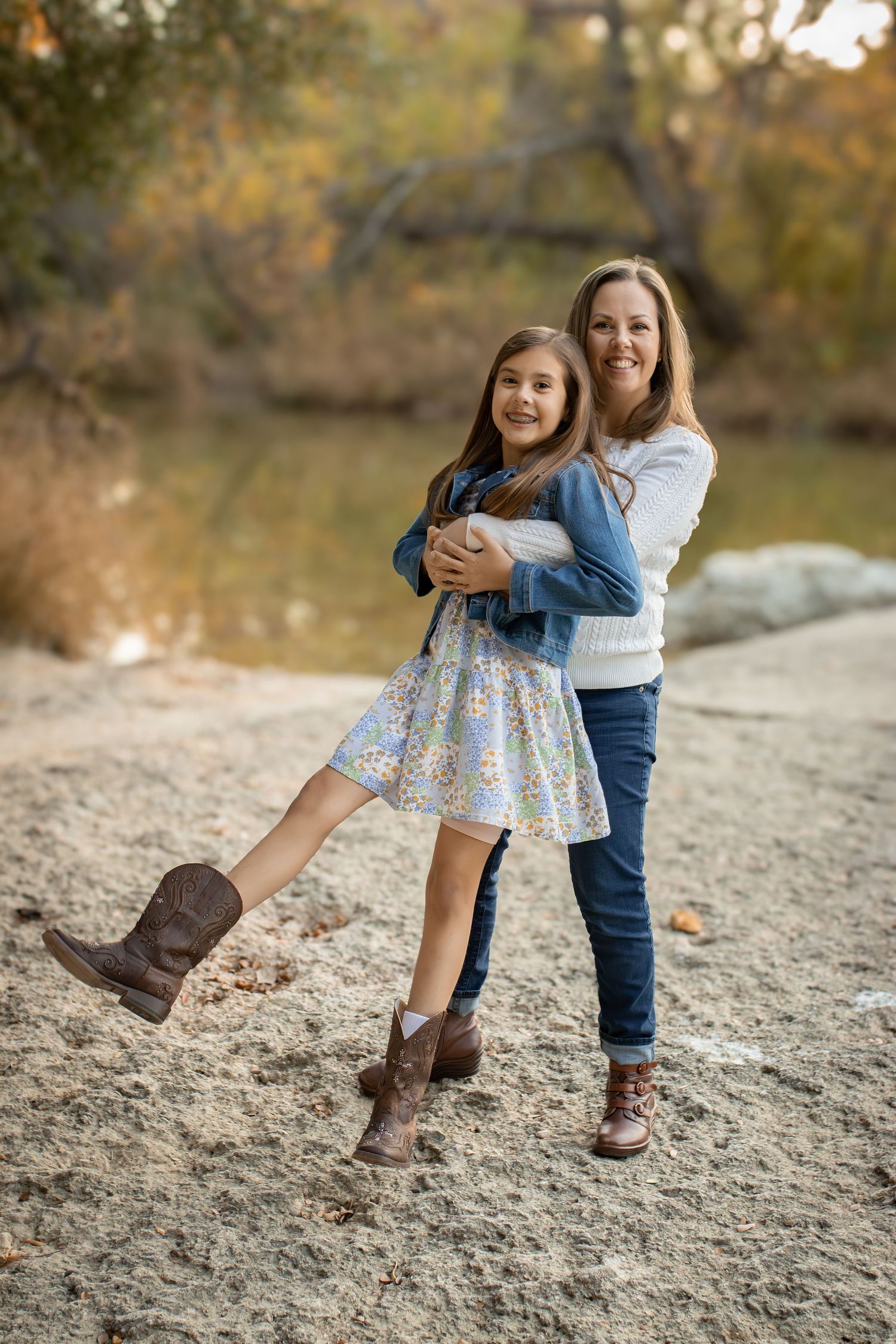 Playful outdoor portrait of parent and child in matching brown boots by autumn lake.
