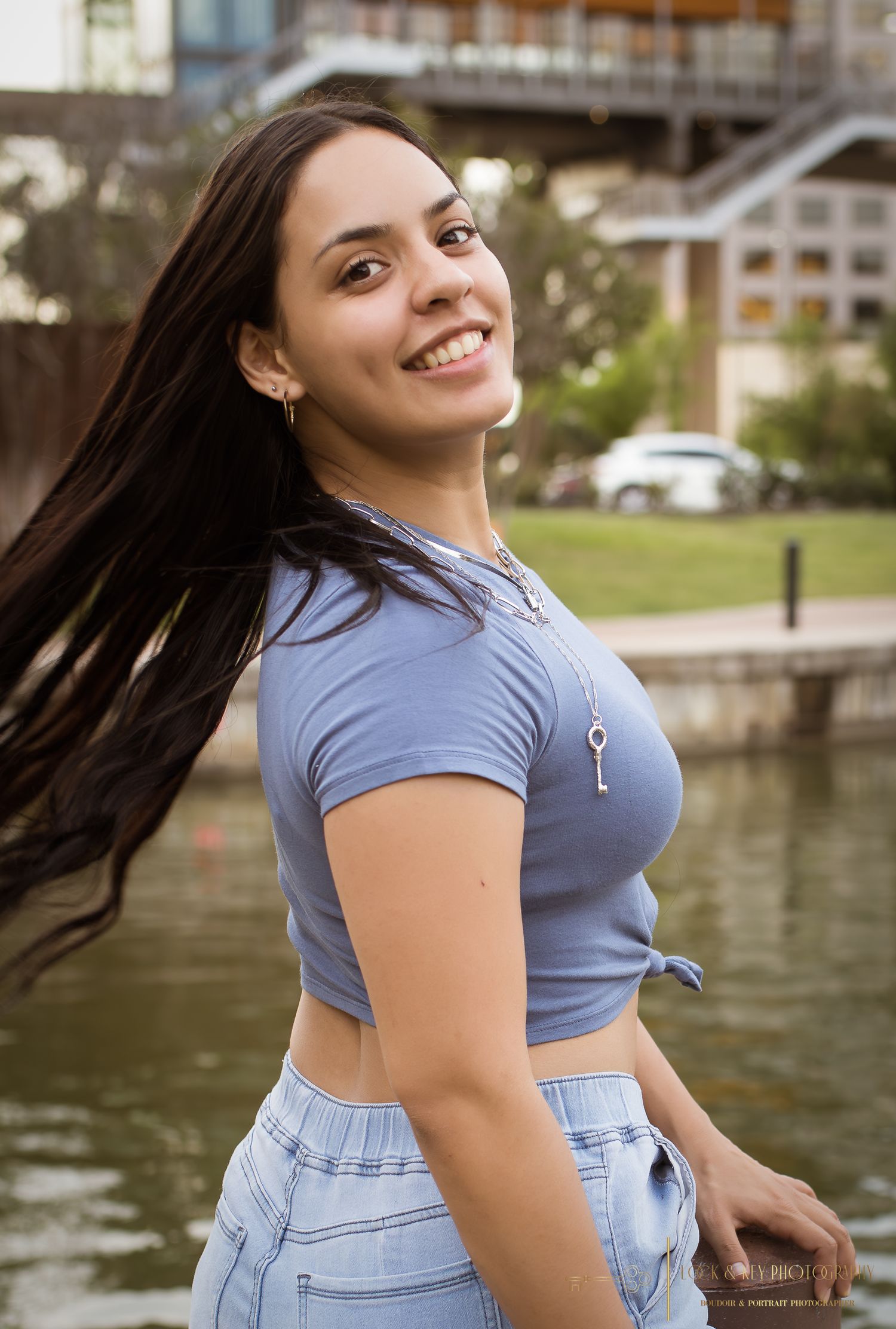 Casual outdoor portrait of woman in blue crop top and jeans by waterfront.